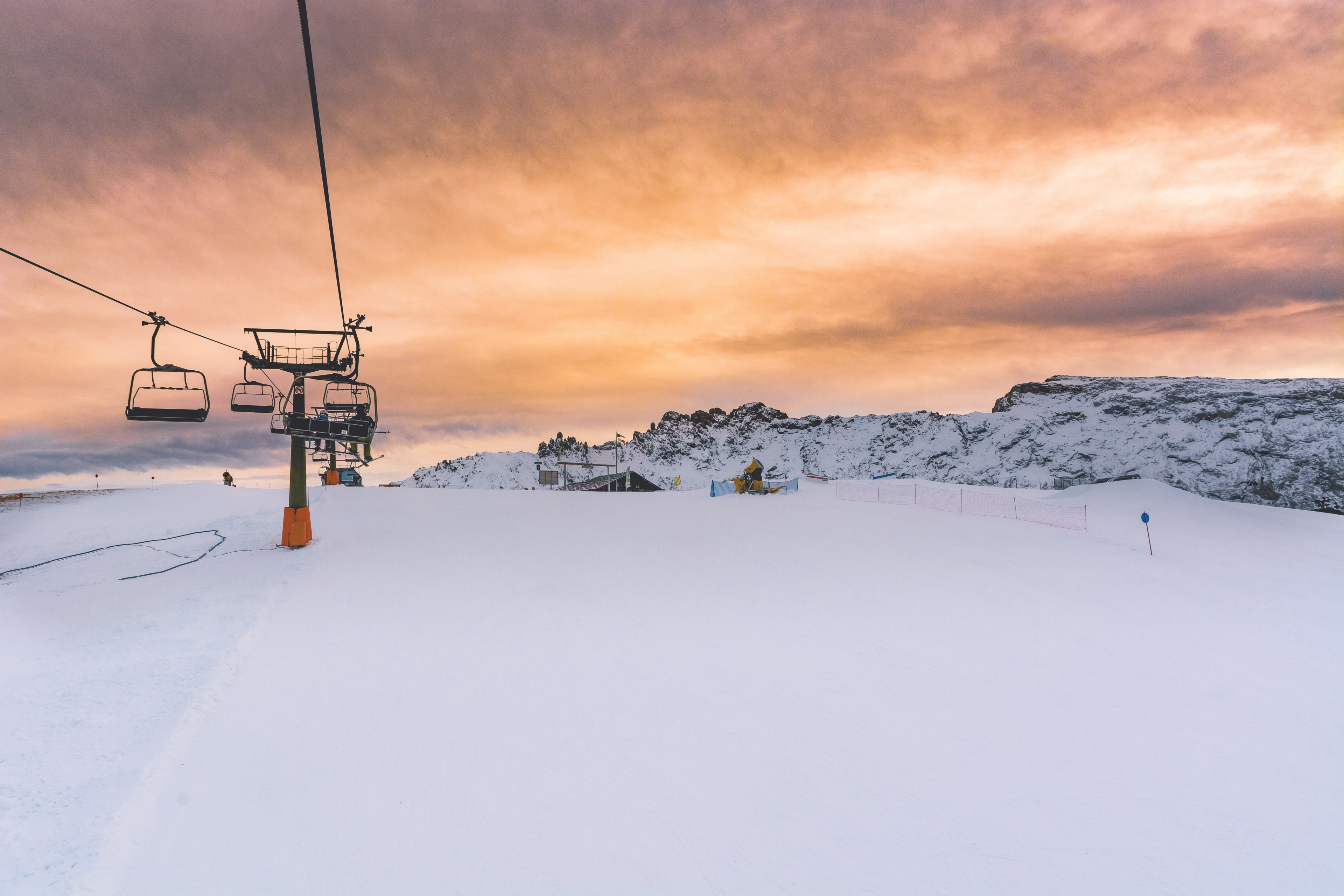 chair lifts on top of a snowcapped seiser alm with an orange cloudy sunset in the distance, sunset over the piste 4k, HD Wallpaper