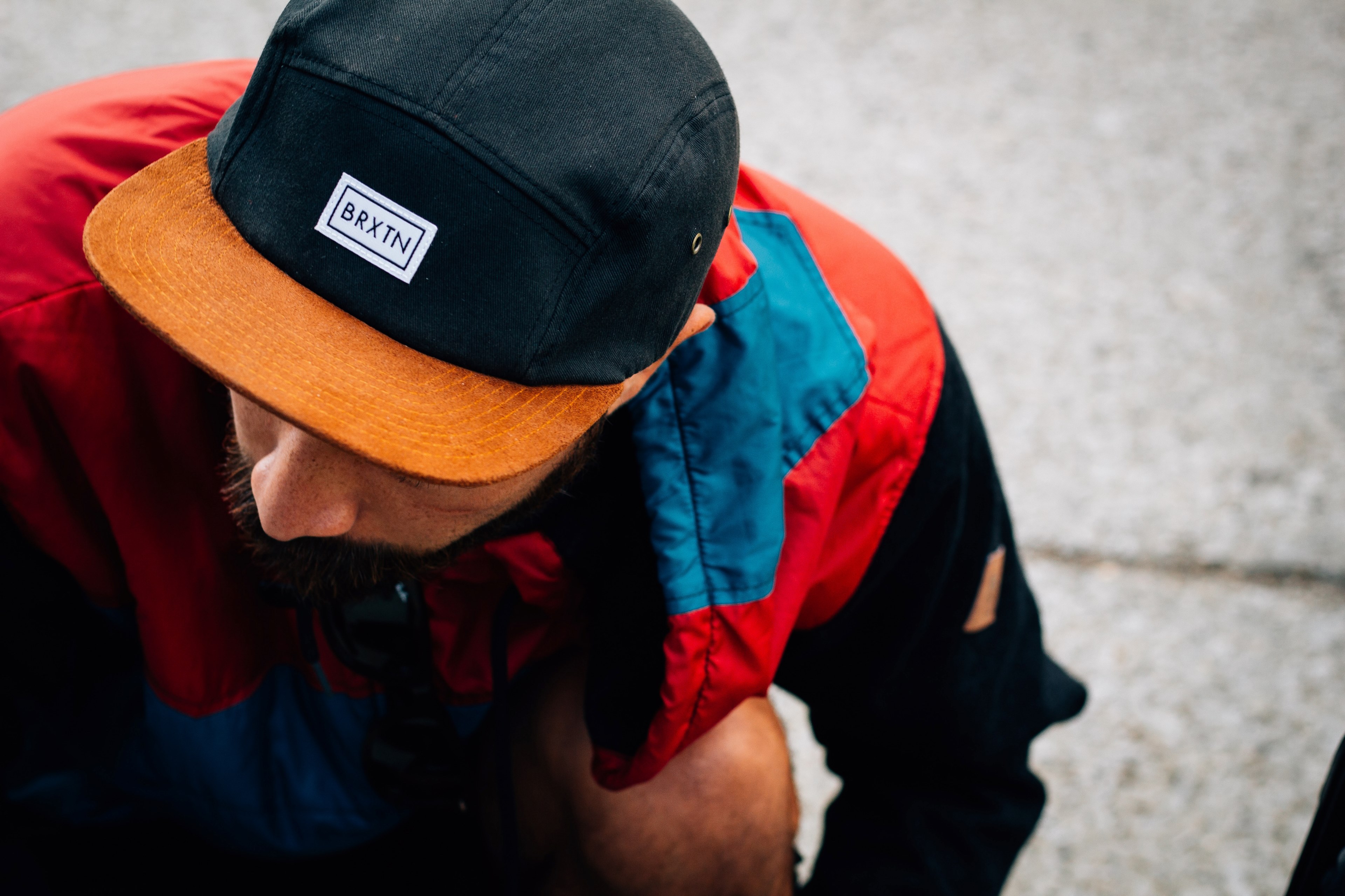 a bearded man in a baseball cap and brightly colored jacket kneels lowering his head, kneeling man in baseball cap 4k, HD Wallpaper