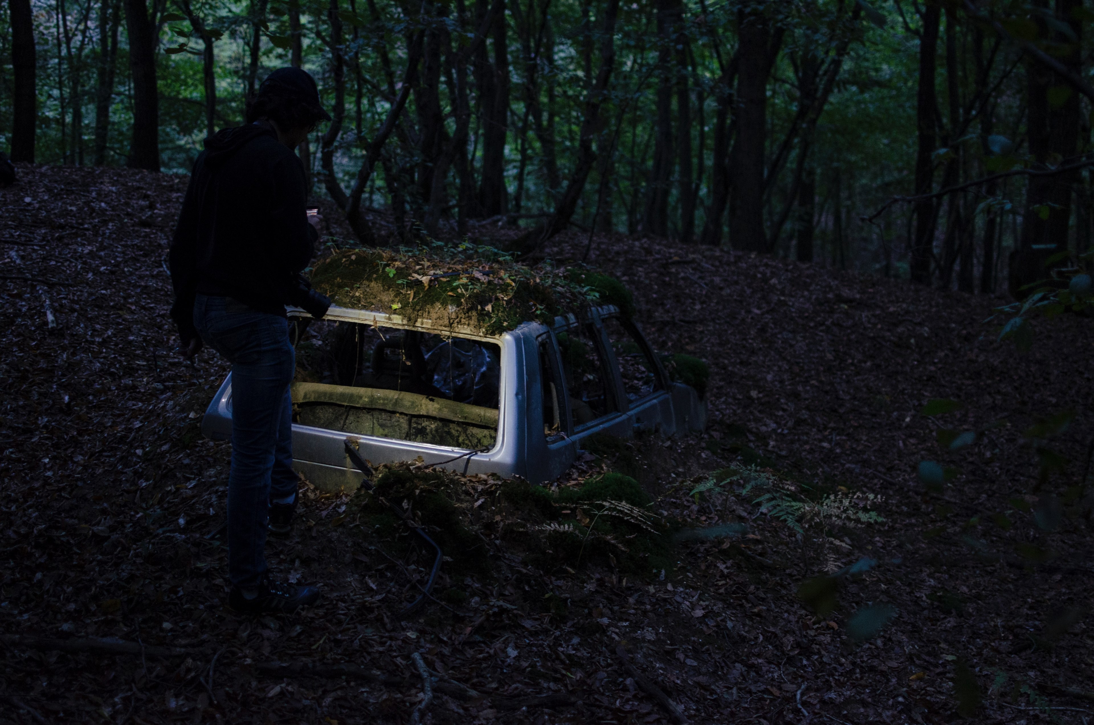 a person near an abandoned car half buried in dirt and leaves in a forest, man car moss leaves 4k, HD Wallpaper