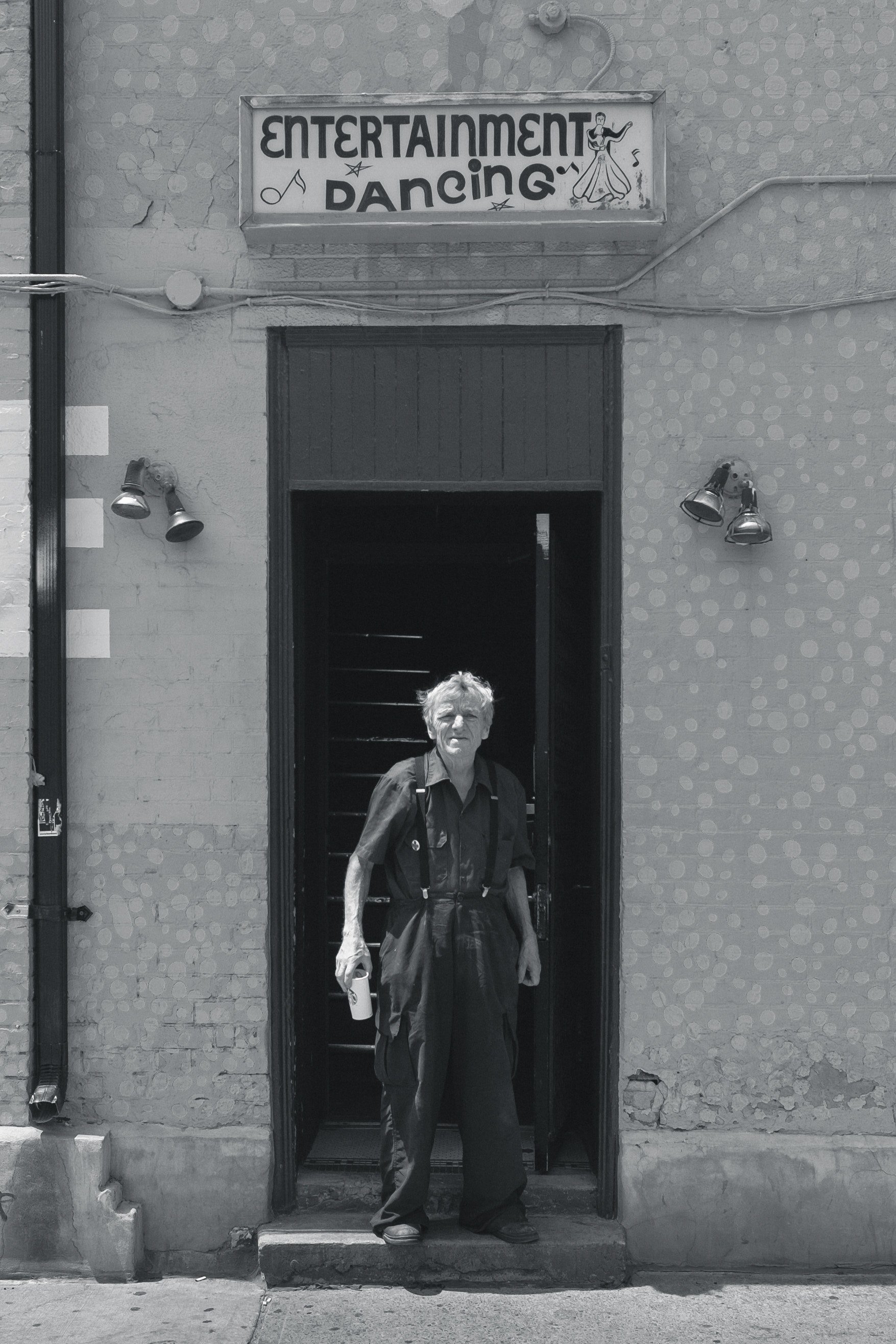 black and white shot of older man in dungarees holding drink in doorway with dancing sign, old man in doorway with drink 4k, Phone HD Wallpaper