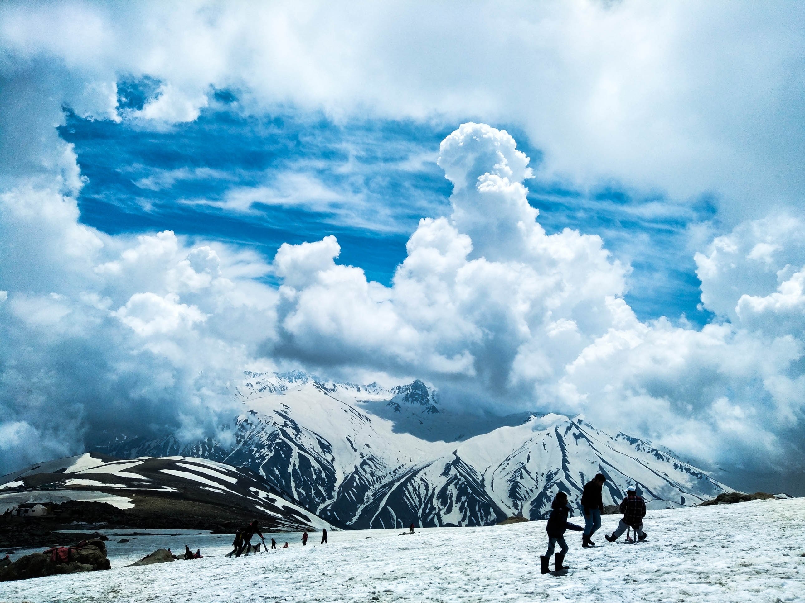 groups of hikers in a snowy field near a snowy mountain massif on a cloudy day, massive clouds over a snow field 4k, HD Wallpaper