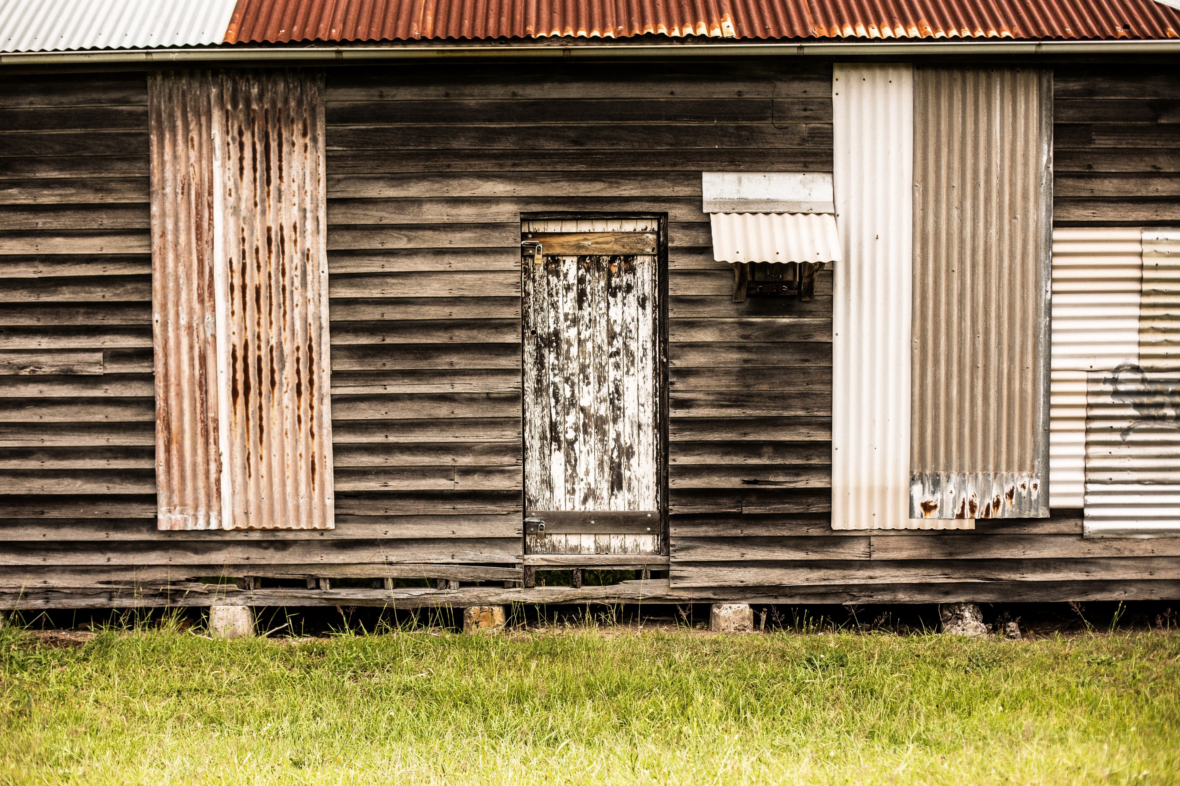 wooden cabin with tin sheet patches and a decaying door in a grassy lawn, old tin and wood cabin 4k, HD Wallpaper