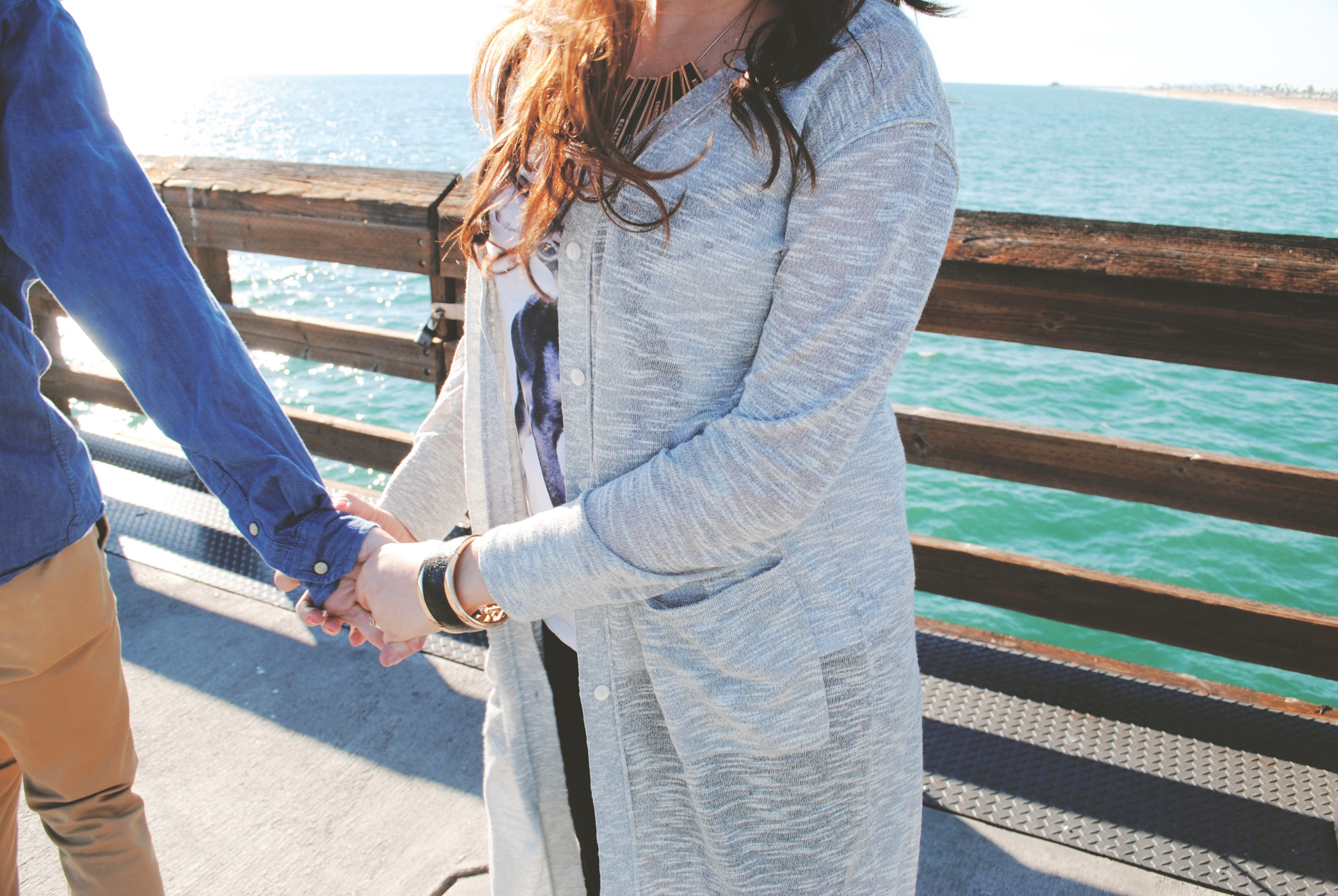 a young woman in a long cardigan holds her partners hand on a pier by the sea, young couple by the sea 4k, HD Wallpaper
