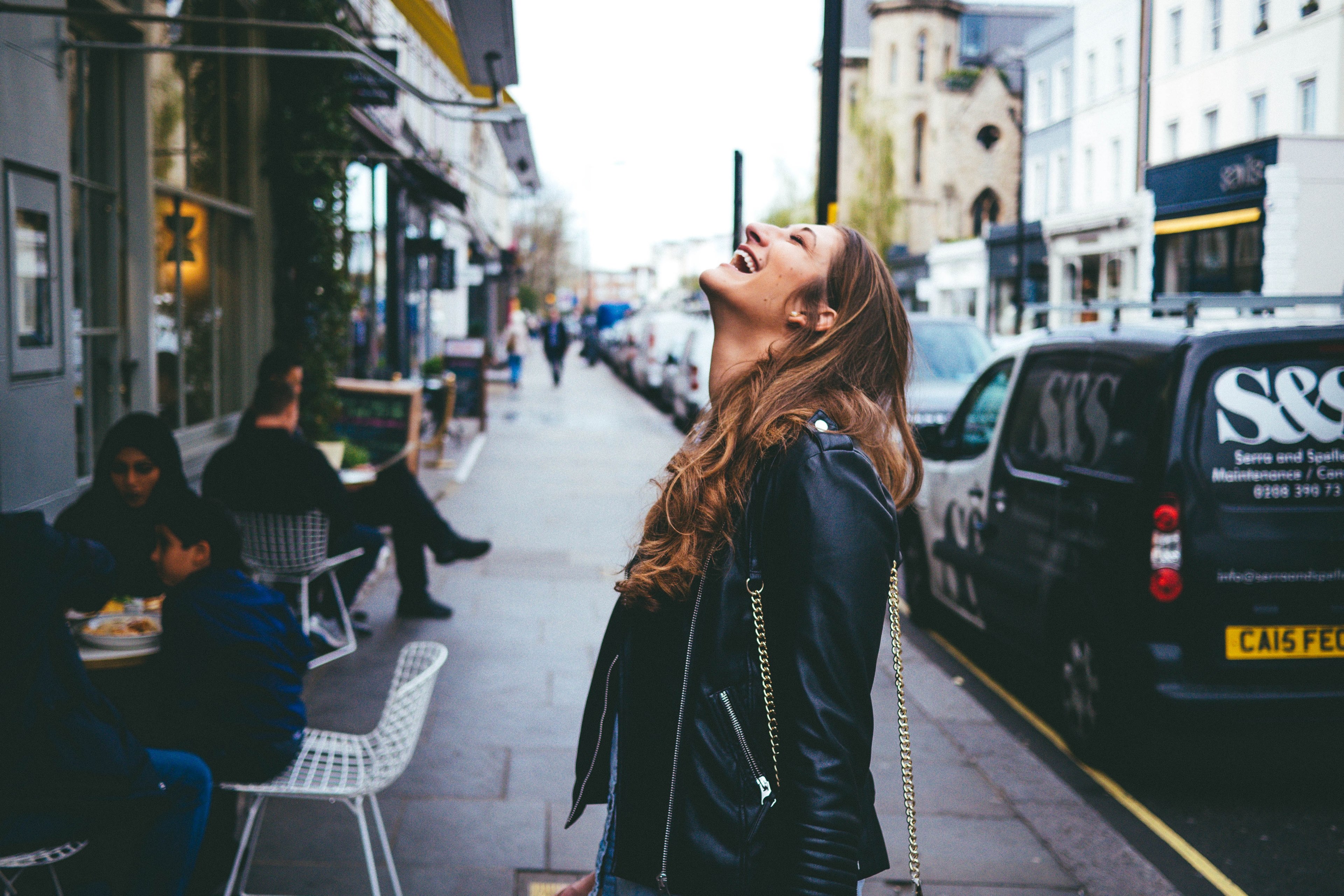 a woman in a leather jacket throws her head back and laughs on a city sidewalk, unbridled joy 4k, HD Wallpaper