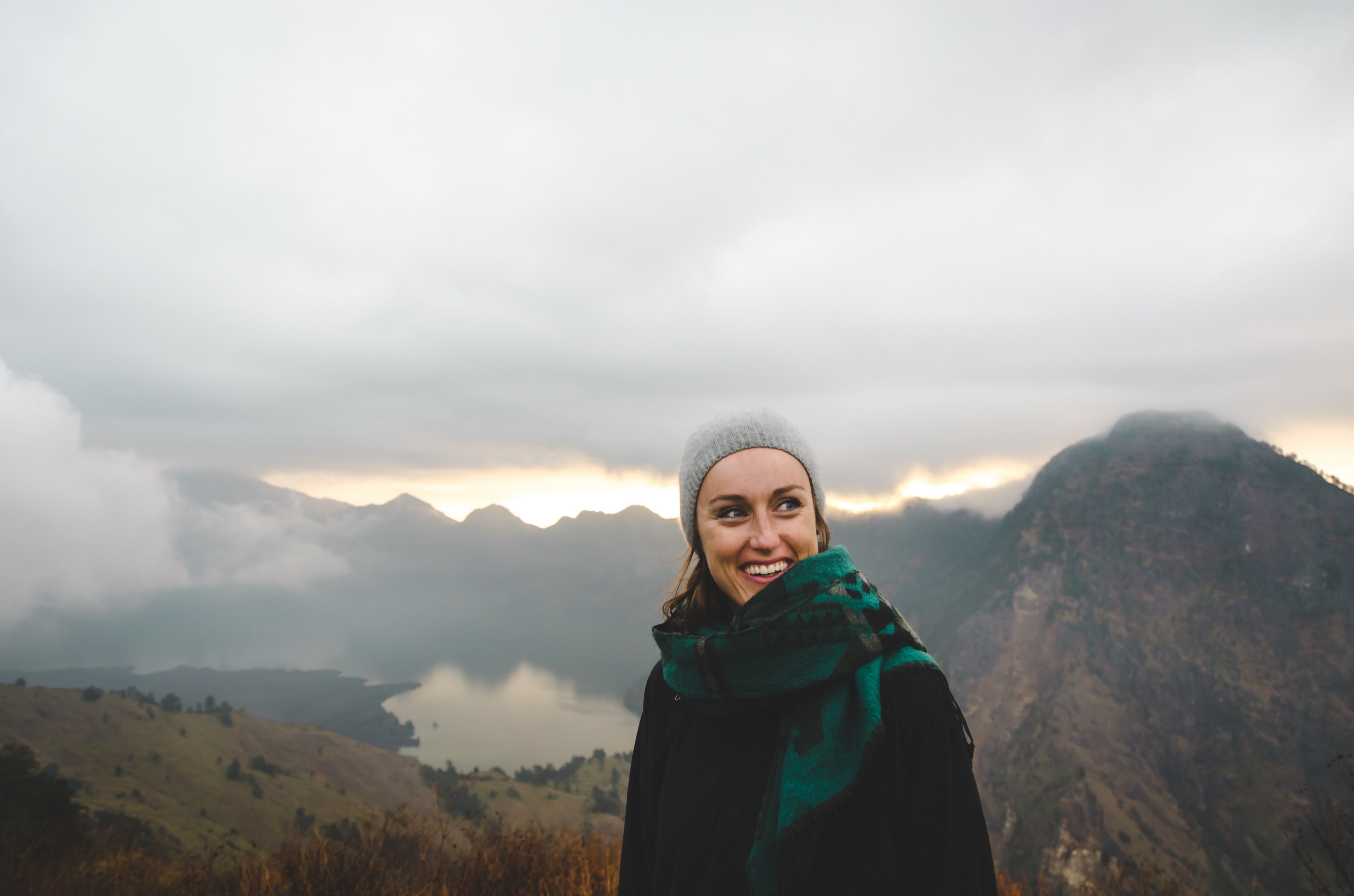 a woman wearing a scarf and a hat smiling atop a cloudy mount rinjani, smiling woman on mount rinjani 4k, HD Wallpaper