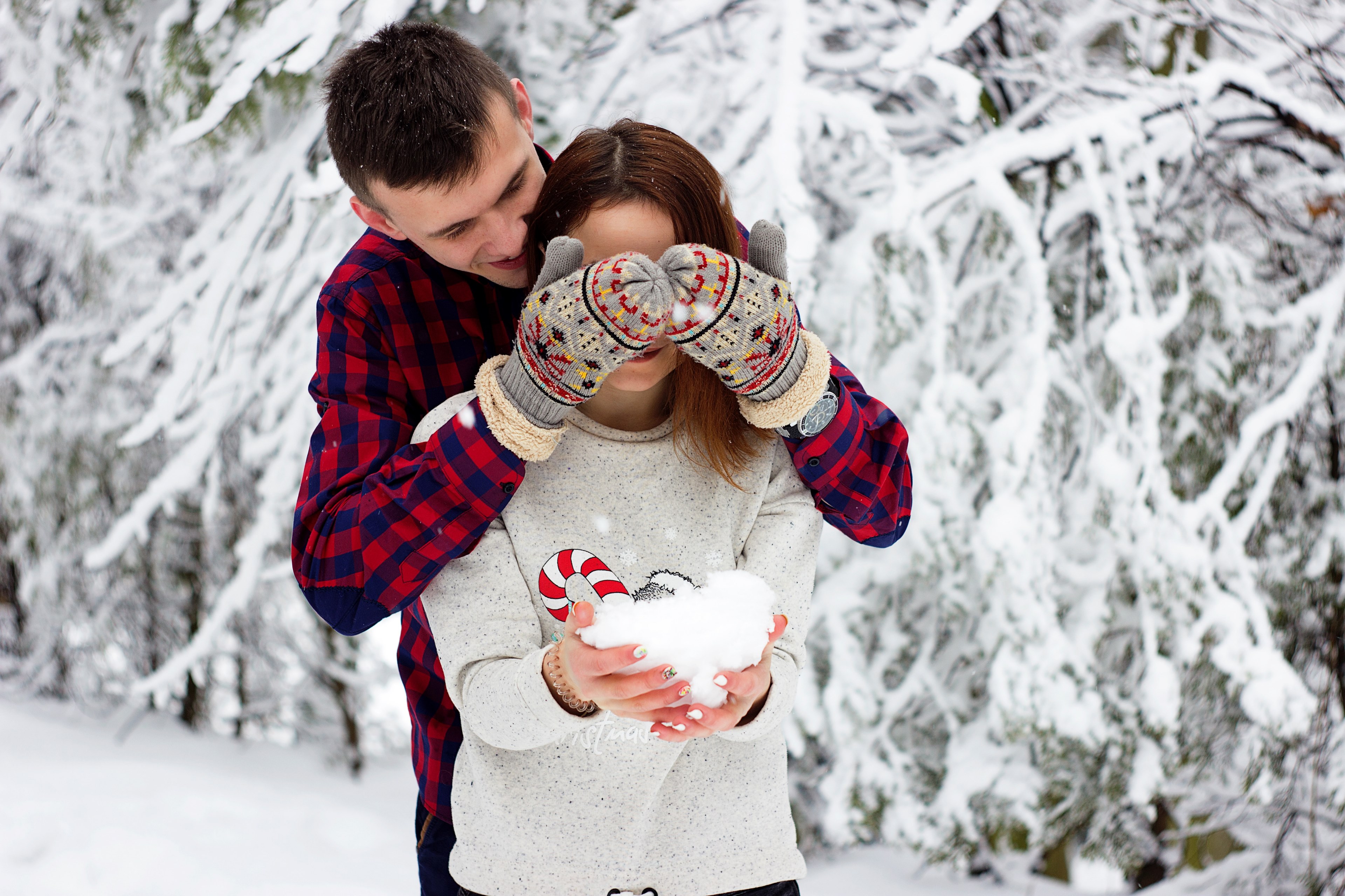 a man stands behind a woman and covers her eyes with his hands in mittens she is laughing and holding a pile of snow in her hands, man and woman laugh in snow 4k, HD Wallpaper