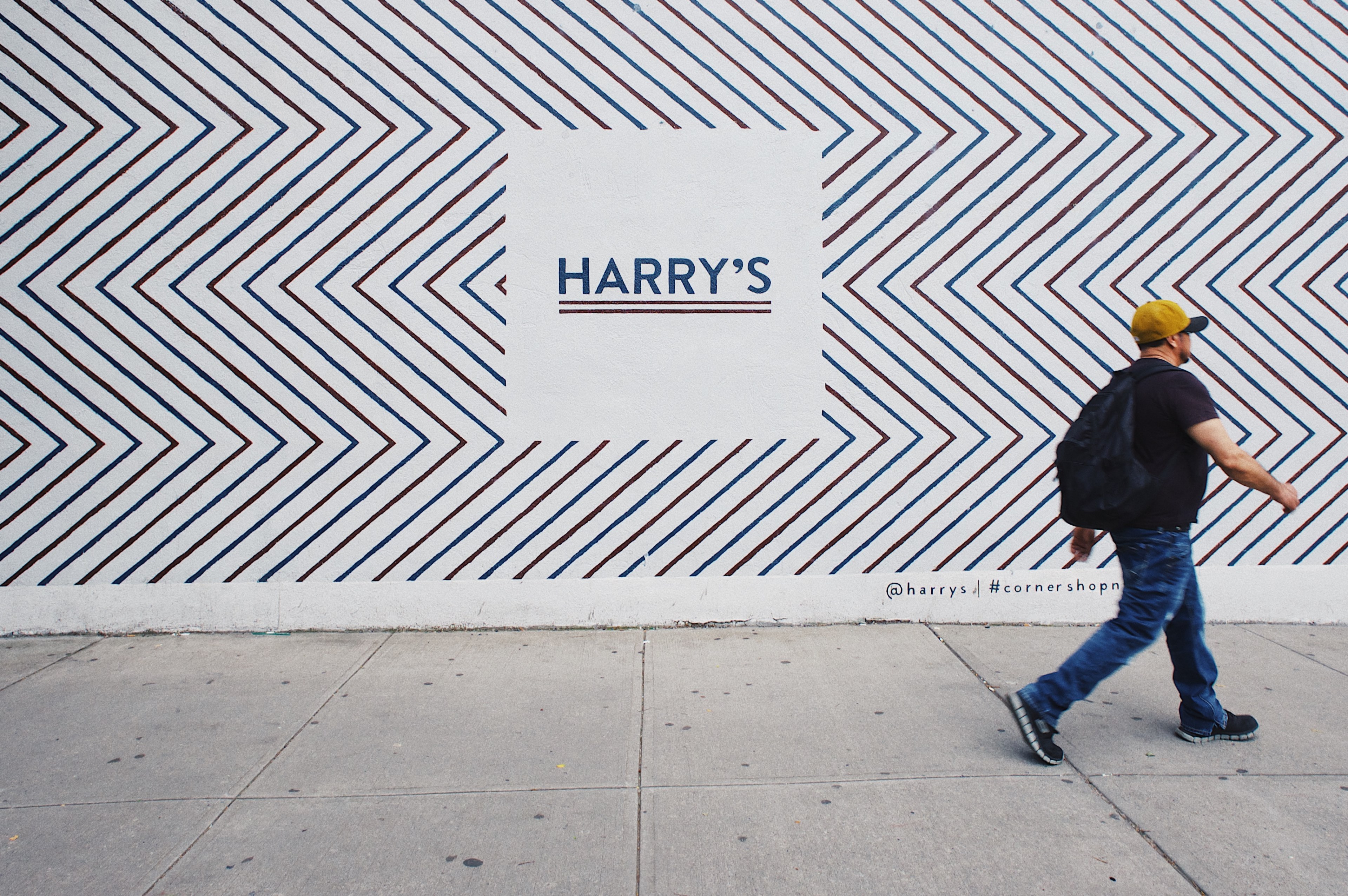 man in hat walks in front of wall with zig zag pattern and a quotharrysquot sign, man walks by harrys sign 4k, HD Wallpaper