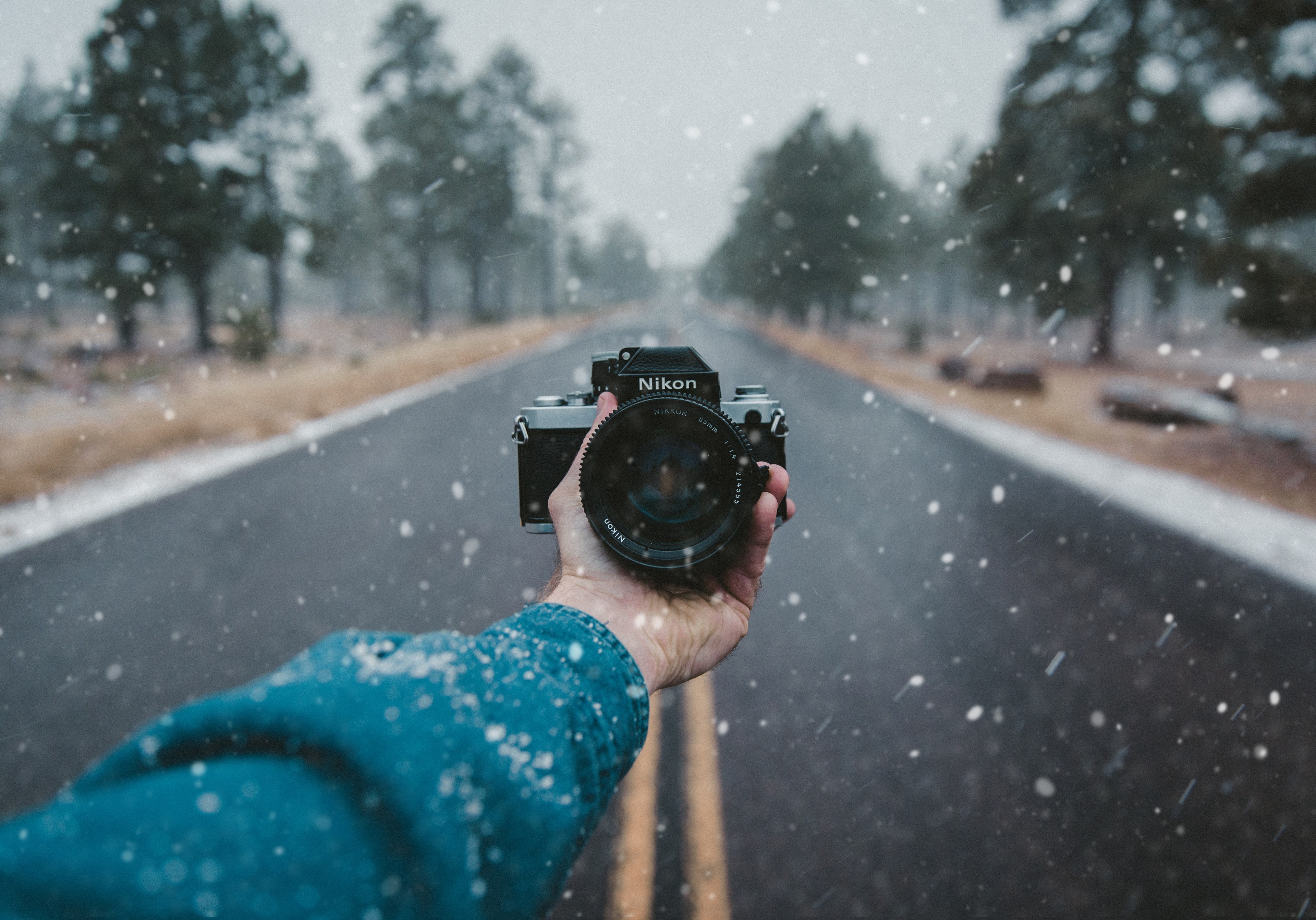 a nikon camera is held facing the photographer standing on an empty road in the snow, _long road nikon 4k, HD Wallpaper