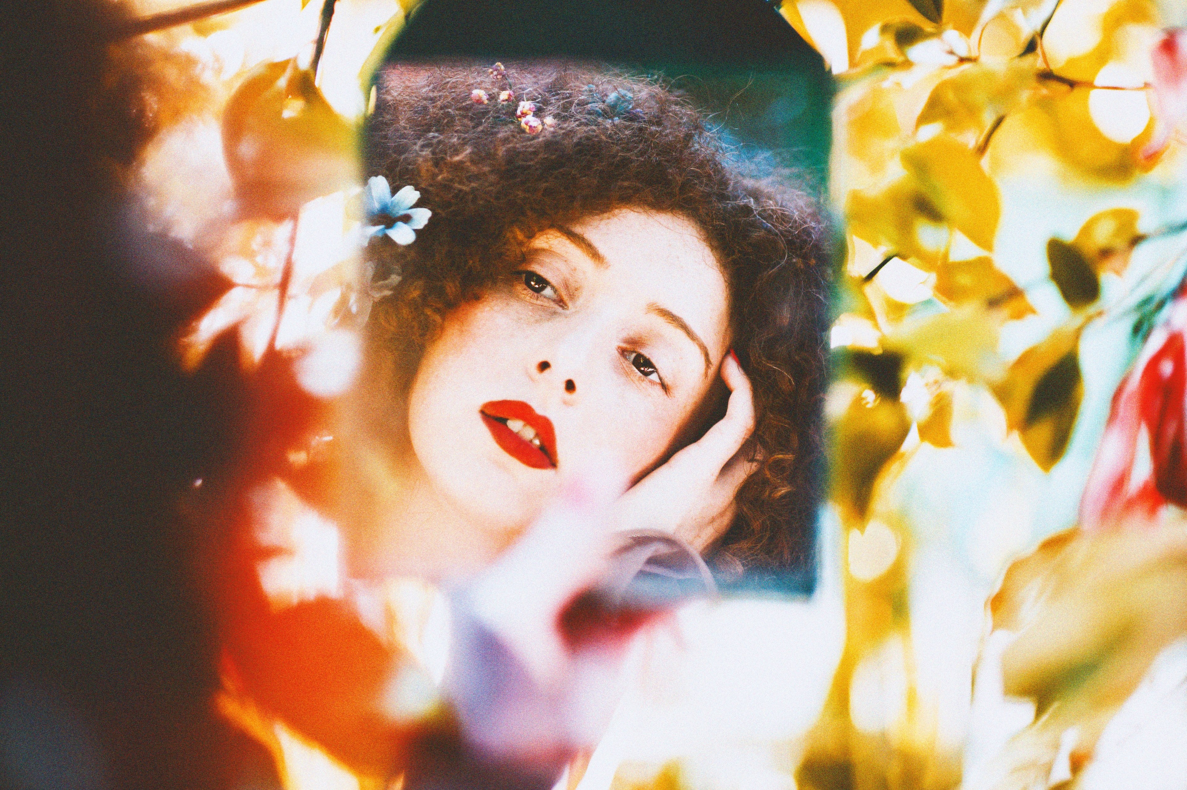 a woman with flowers in her curly hair looks at her reflection in a hand mirror, looking at her reflection 4k, HD Wallpaper