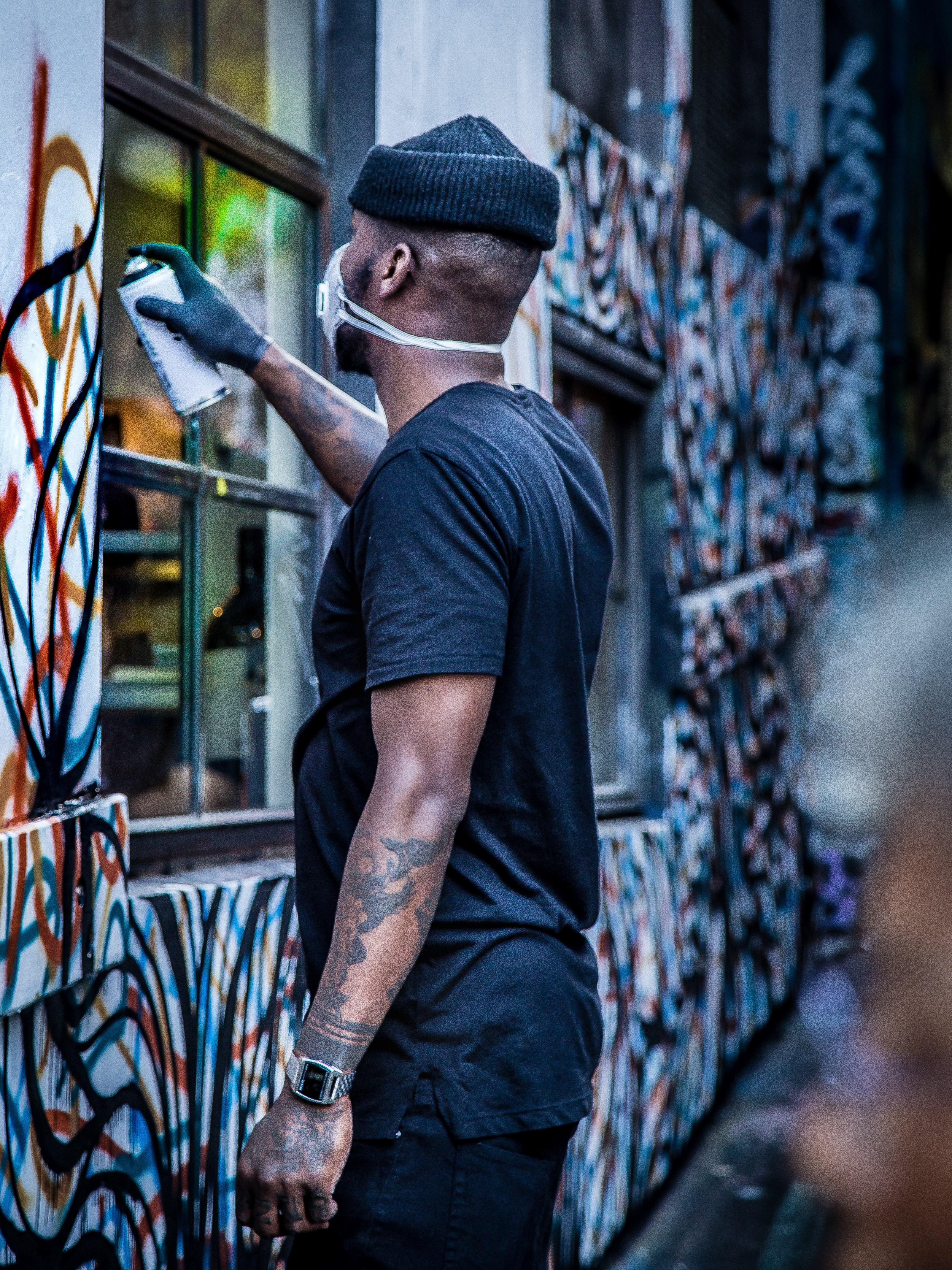 tattooed man wearing a hat and facemask spraypainting graffiti on a building wall on hosier lane, artist spray paints building 4k, Phone HD Wallpaper