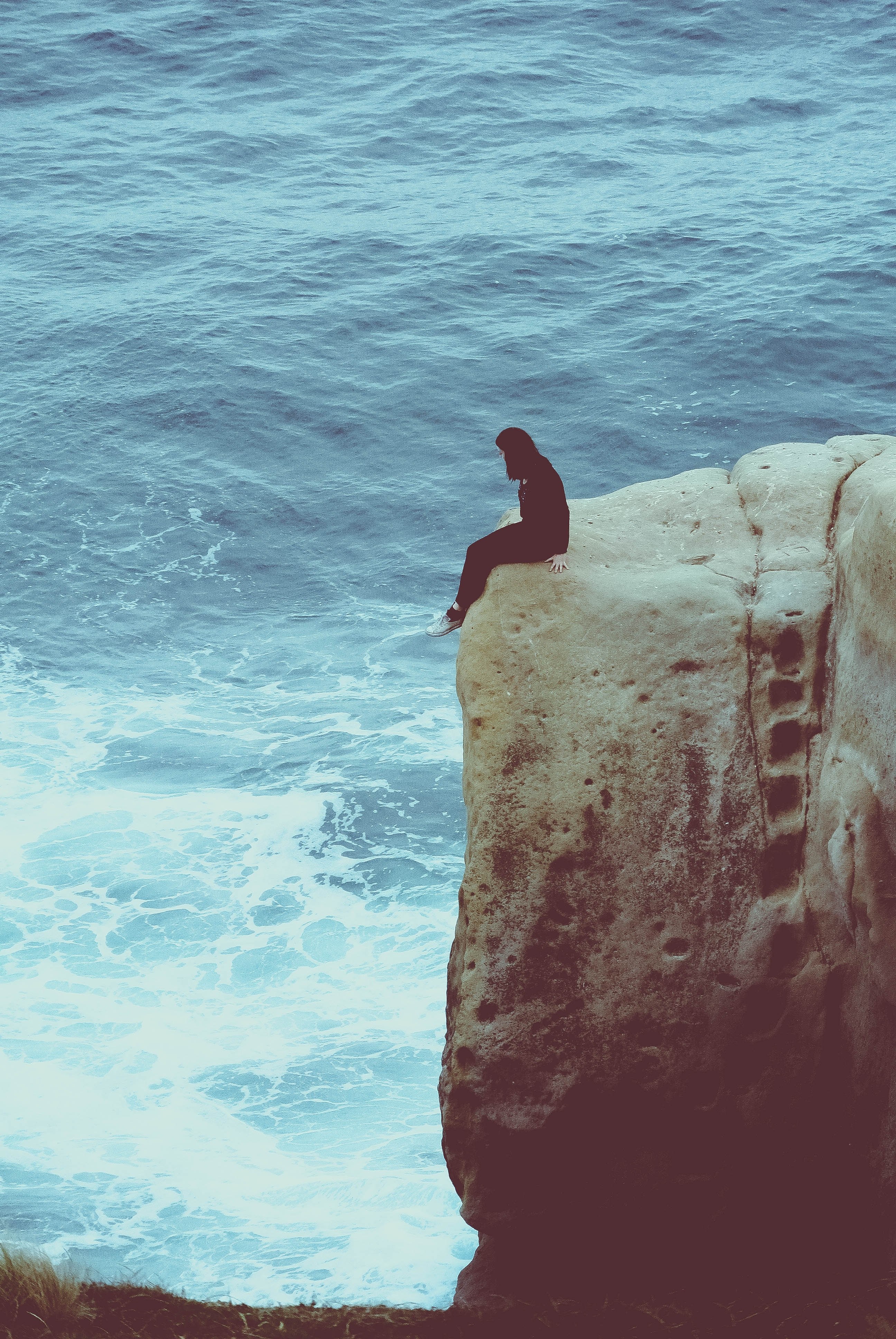 woman sitting on the rock above the ocean at tunnel beach, danger 4k, Phone HD Wallpaper