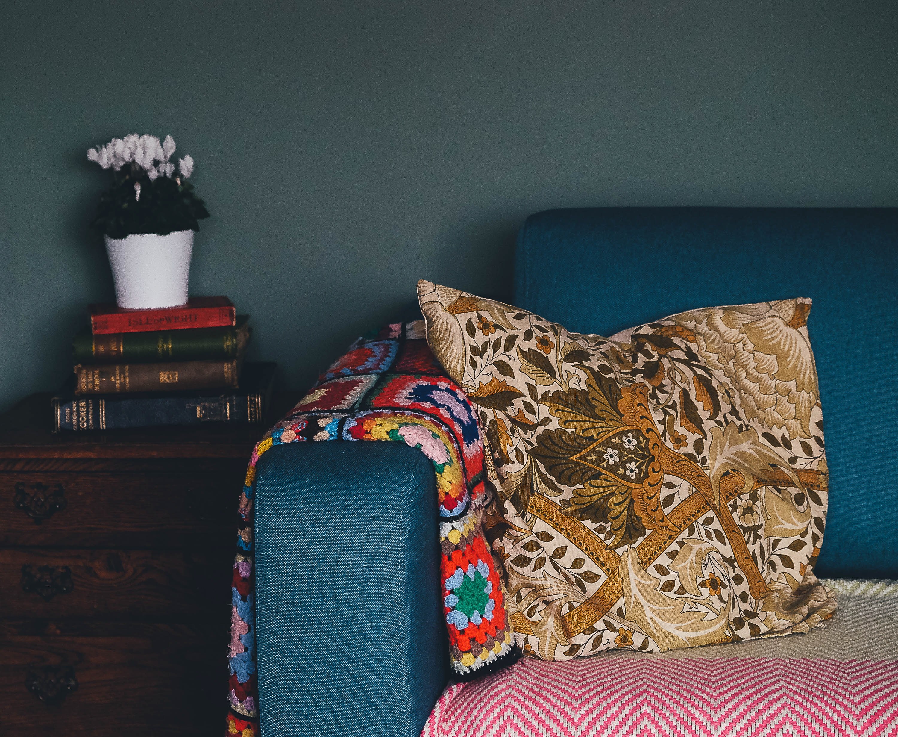 a blue sofa colored blankets brown patterned pillow wooden end table stack of books and potted plant in a living room, cosy corner 4k, HD Wallpaper