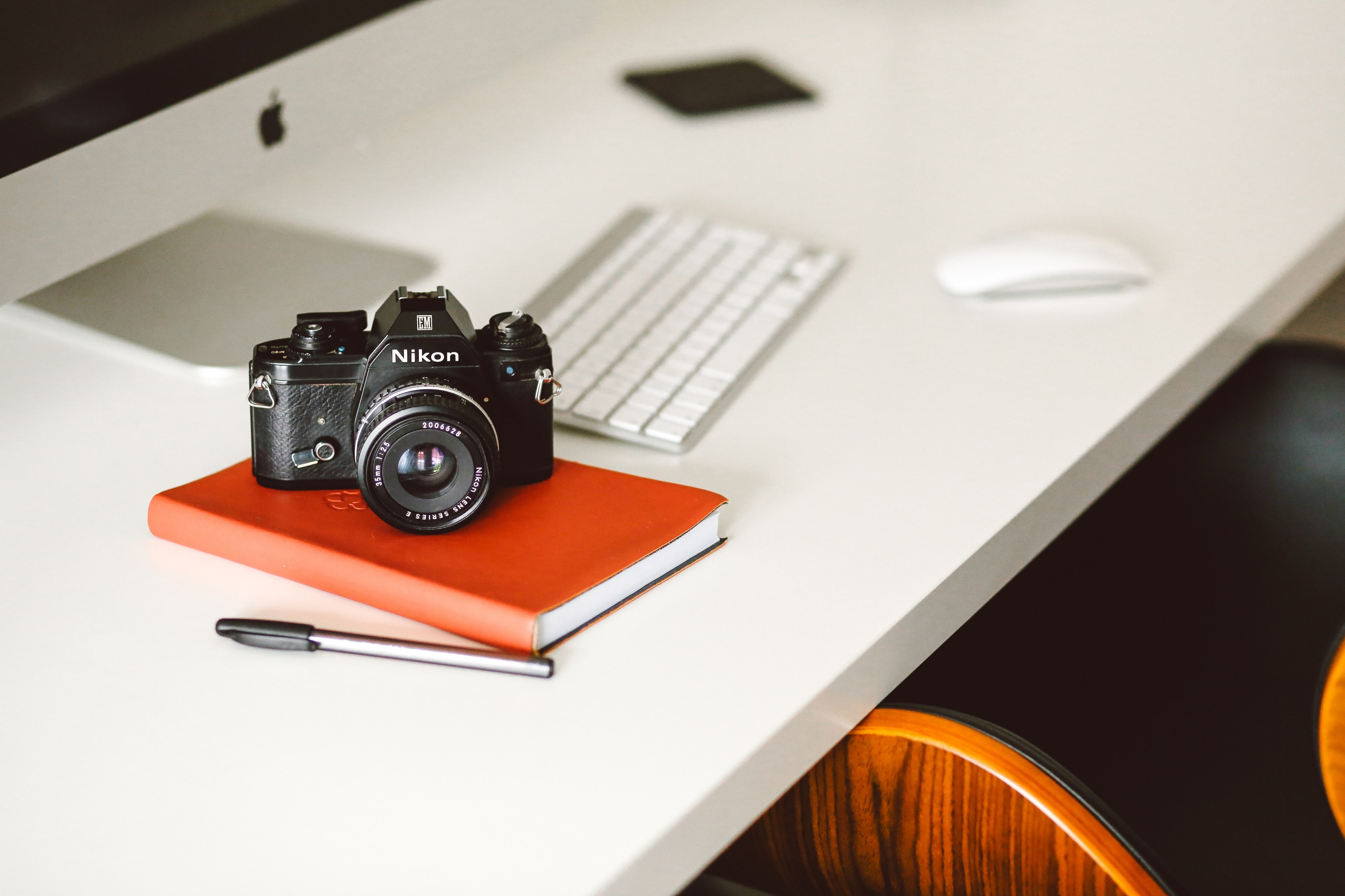 nikon camera on top of orange notebook on desk with desktop computer and mouse, camera desk computer notepad life 4k, HD Wallpaper