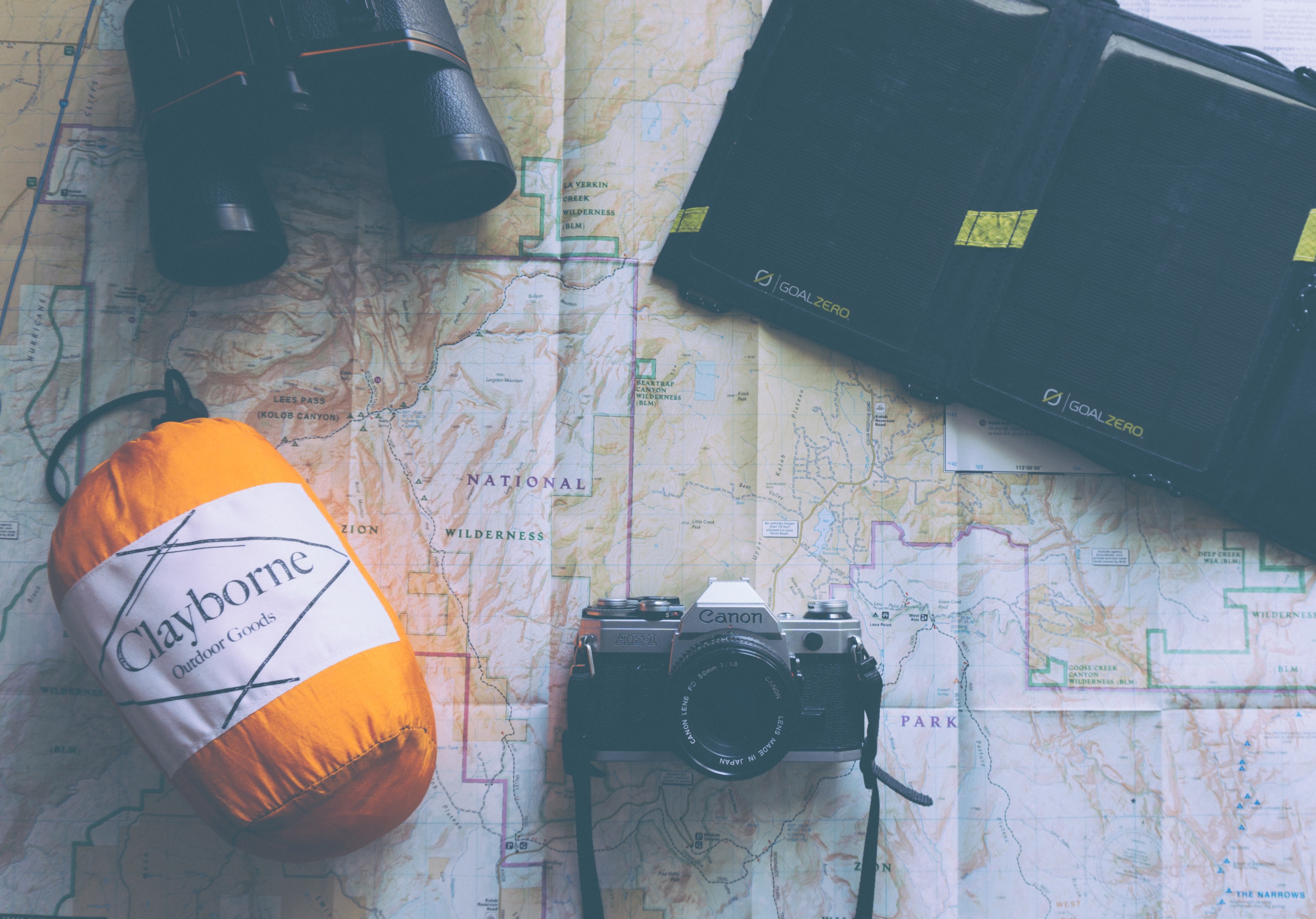 a solar powered portable battery canon camera binoculars and claybourne outdoor goods pack on a map, map flatlay 4k, HD Wallpaper