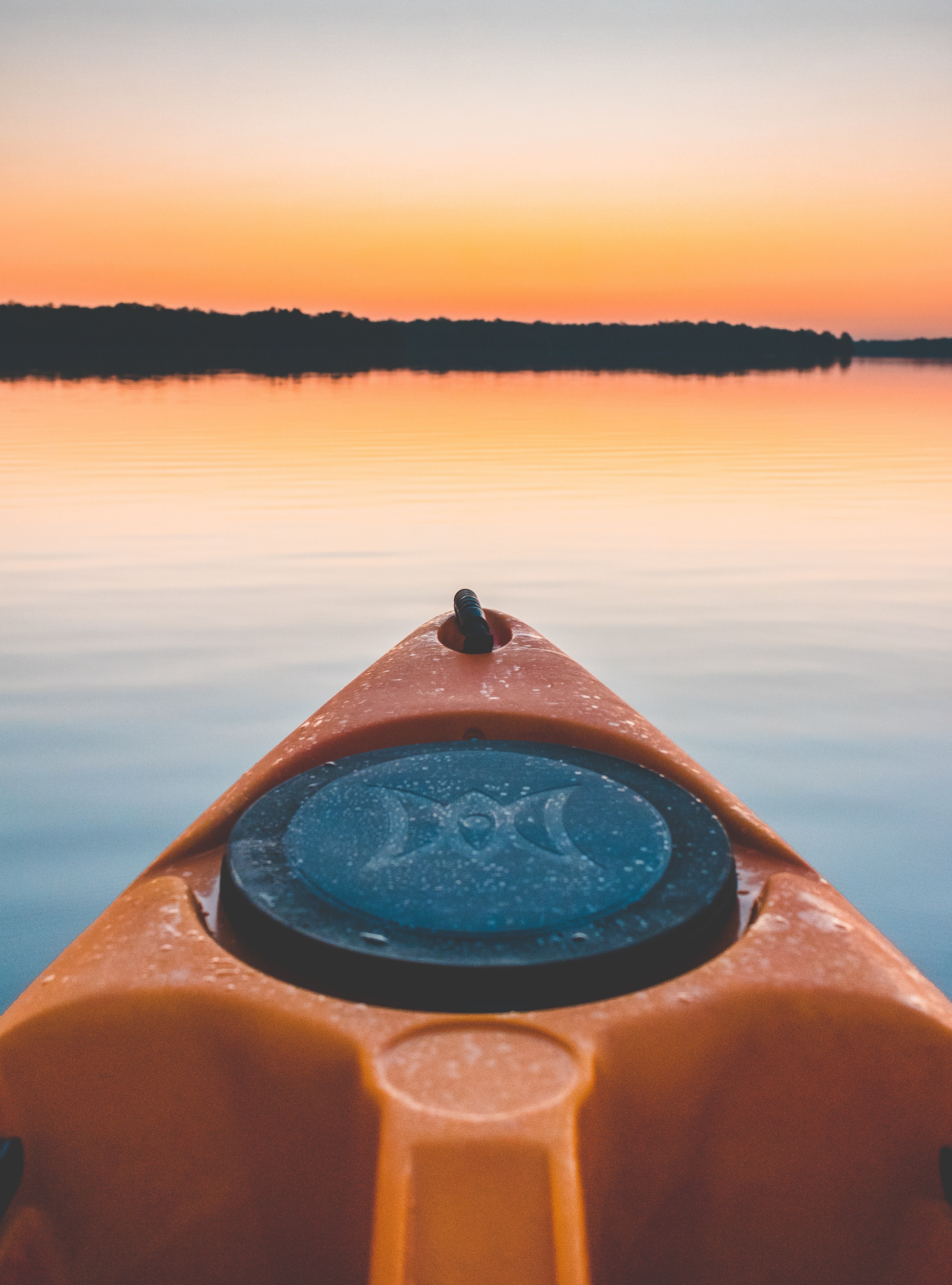 front point of an orange and black kayak on calm water trees in the distance at sunset, floating on water 4k, Phone HD Wallpaper