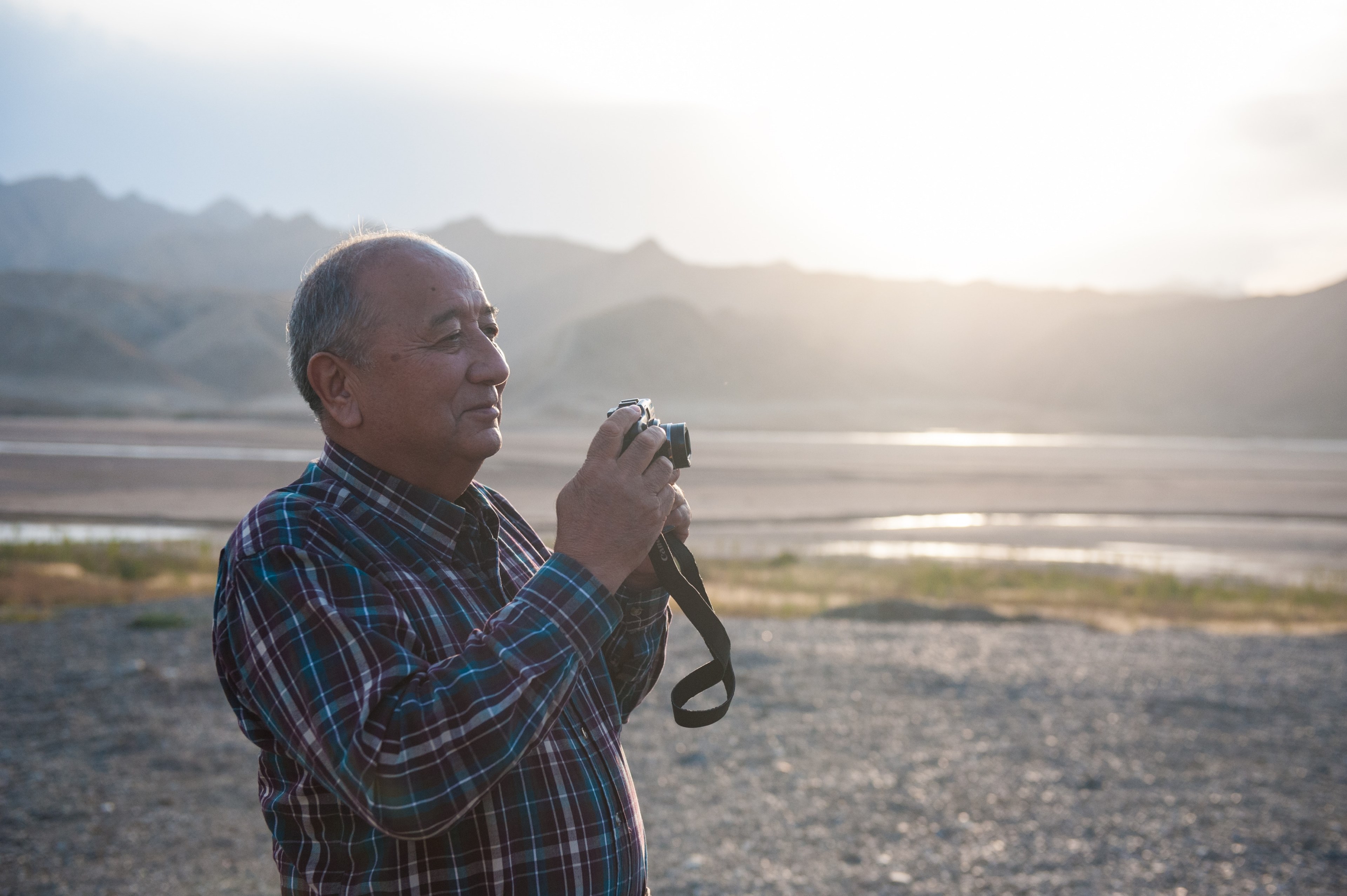 old man in checkered shirt holding a photo camera at torgayti village, old man holding camera 4k, HD Wallpaper