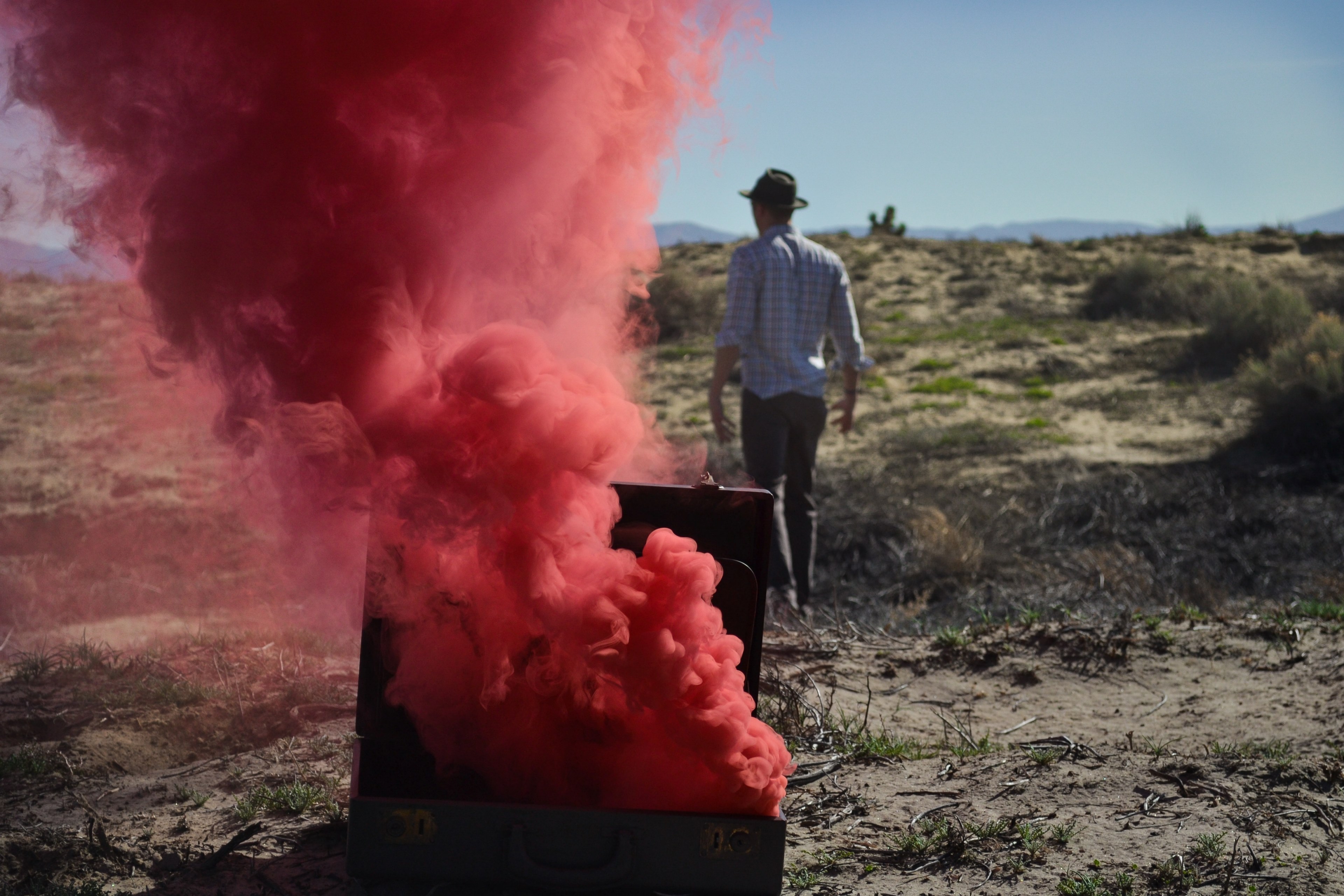 a man in a black hat walking away from a suitcase with red smoke coming out of it, m o v i n g o n 4k, HD Wallpaper
