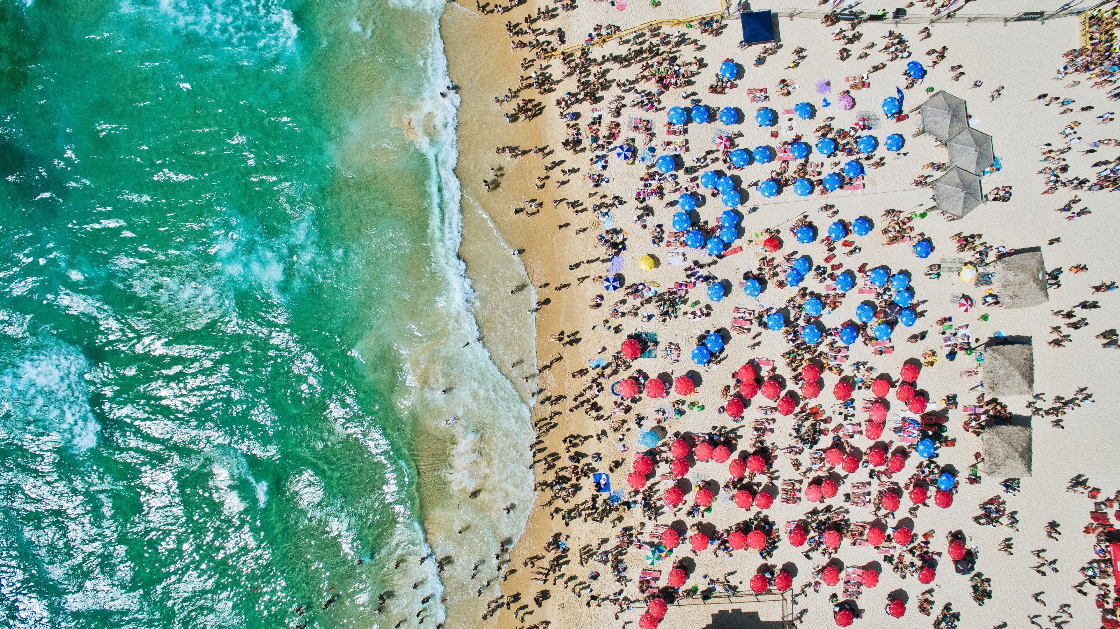 an aerial shot of a crowded beach with vacationers sheltering from the sun under red and blue umbrellas, vertical from above 4k, HD Wallpaper