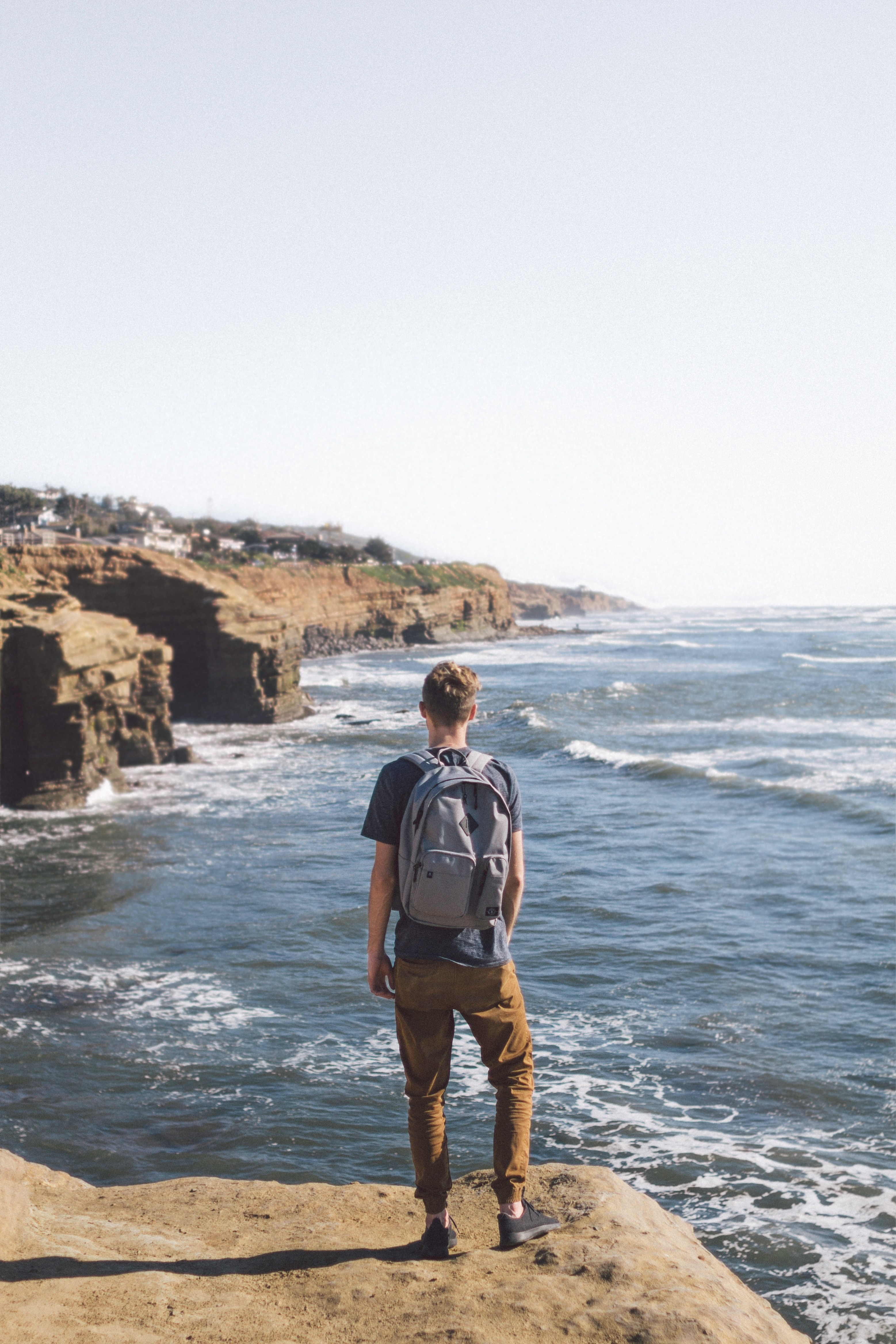 man in pants with backpack stands by sunset cliffs, at the edge 4k, Phone HD Wallpaper