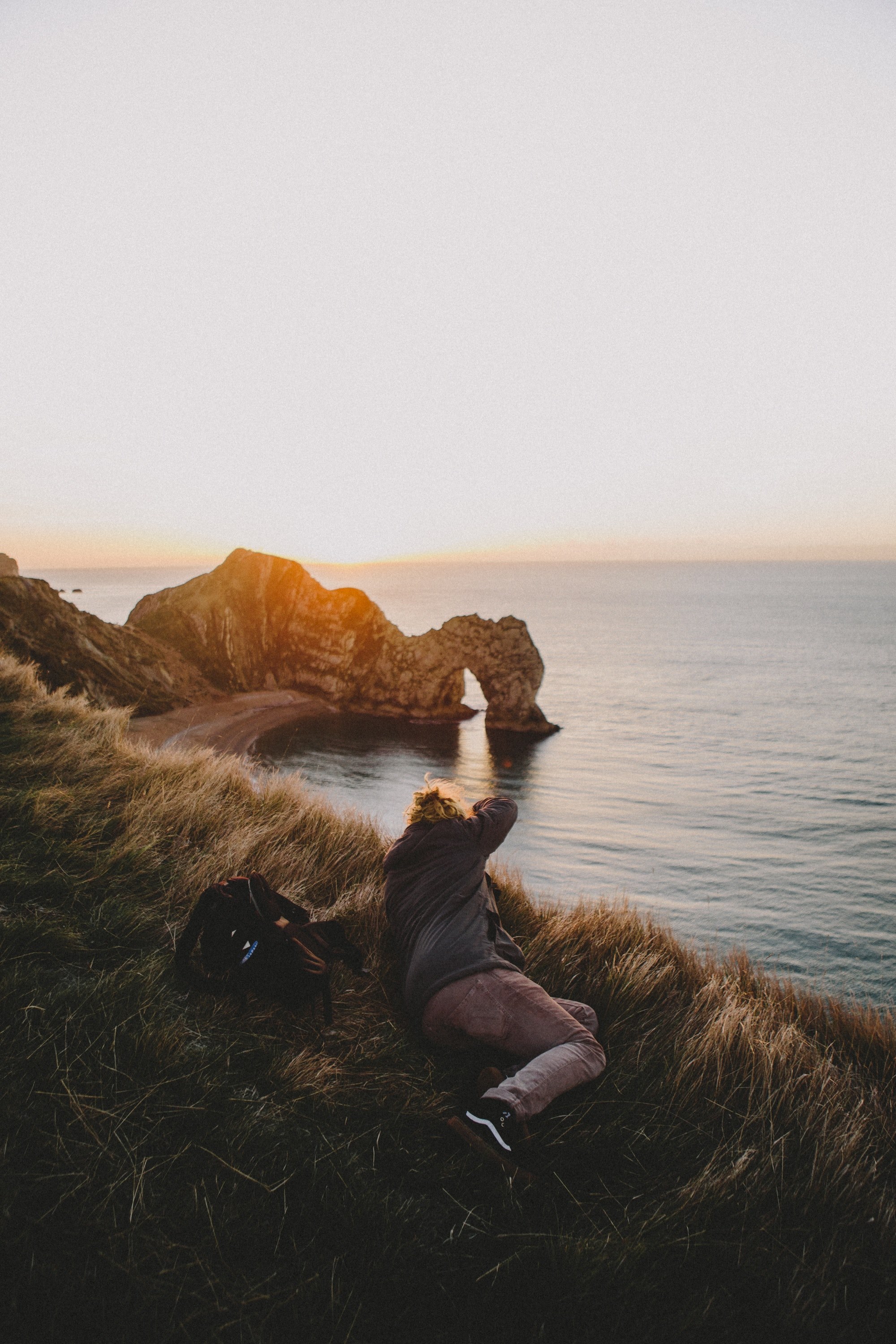 photographer lying on the grass capturing the durdle door arch on the cove during golden hour, photographing durdle door arch 4k, Phone HD Wallpaper