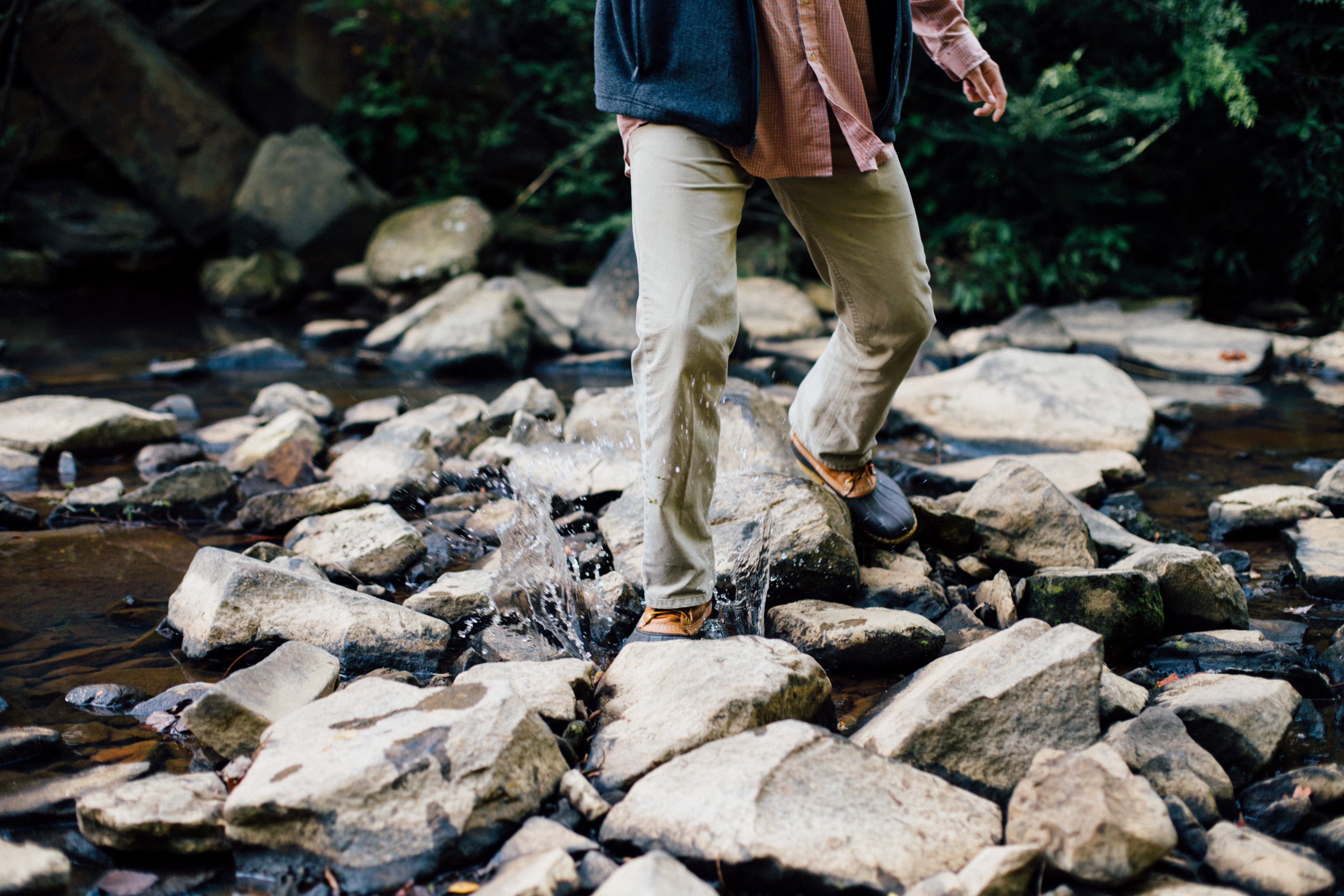 a man splashing across a stream in duck boots and a vest, splashing water between rocks 4k, HD Wallpaper