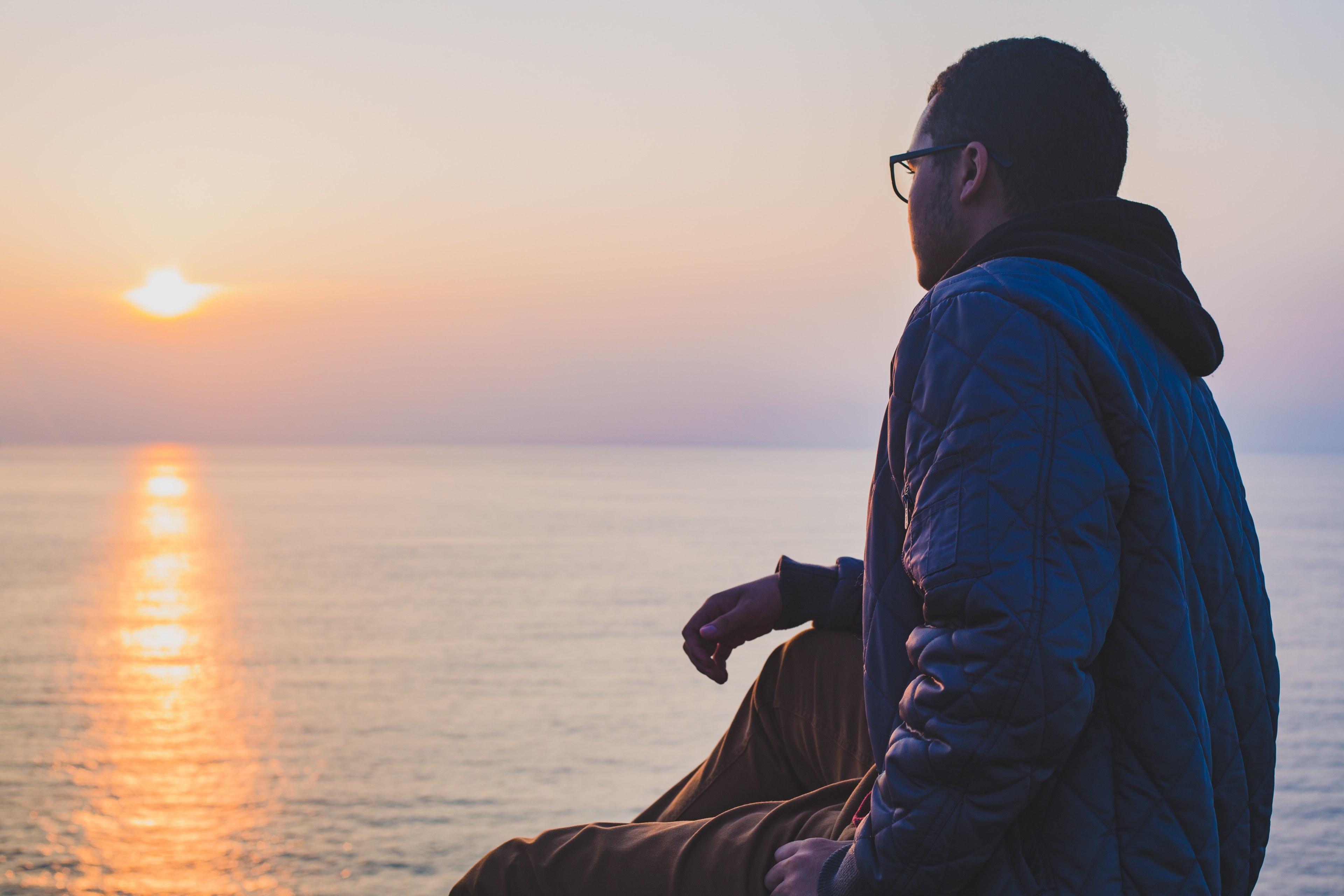 a person with glasses and a hood sits overlooking a sunset on the ocean, person watching the sunset 4k, HD Wallpaper