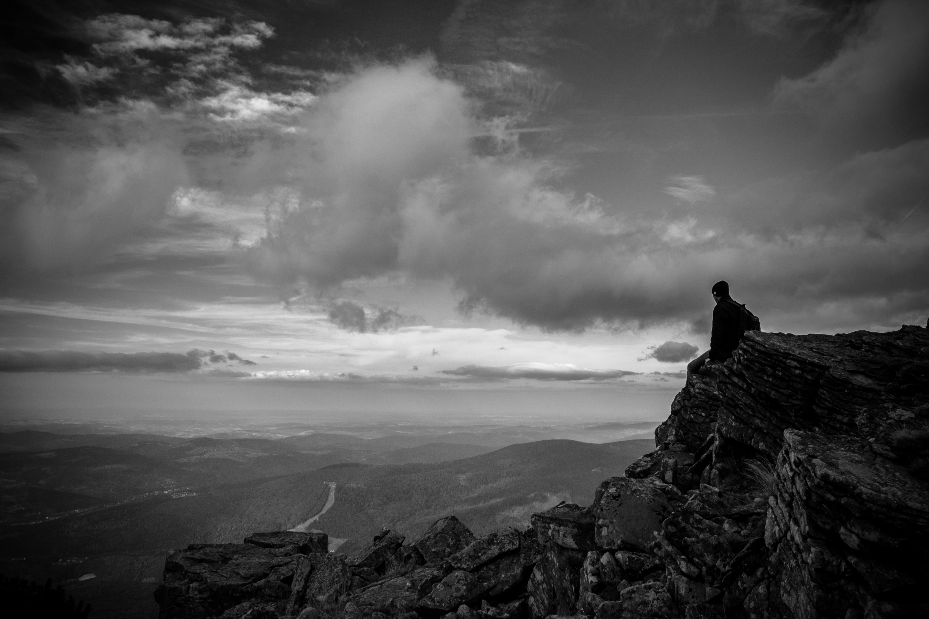 a lone man sitting on jagged rocks overlooking a fertile valley, man sitting on rock ledge 4k, HD Wallpaper