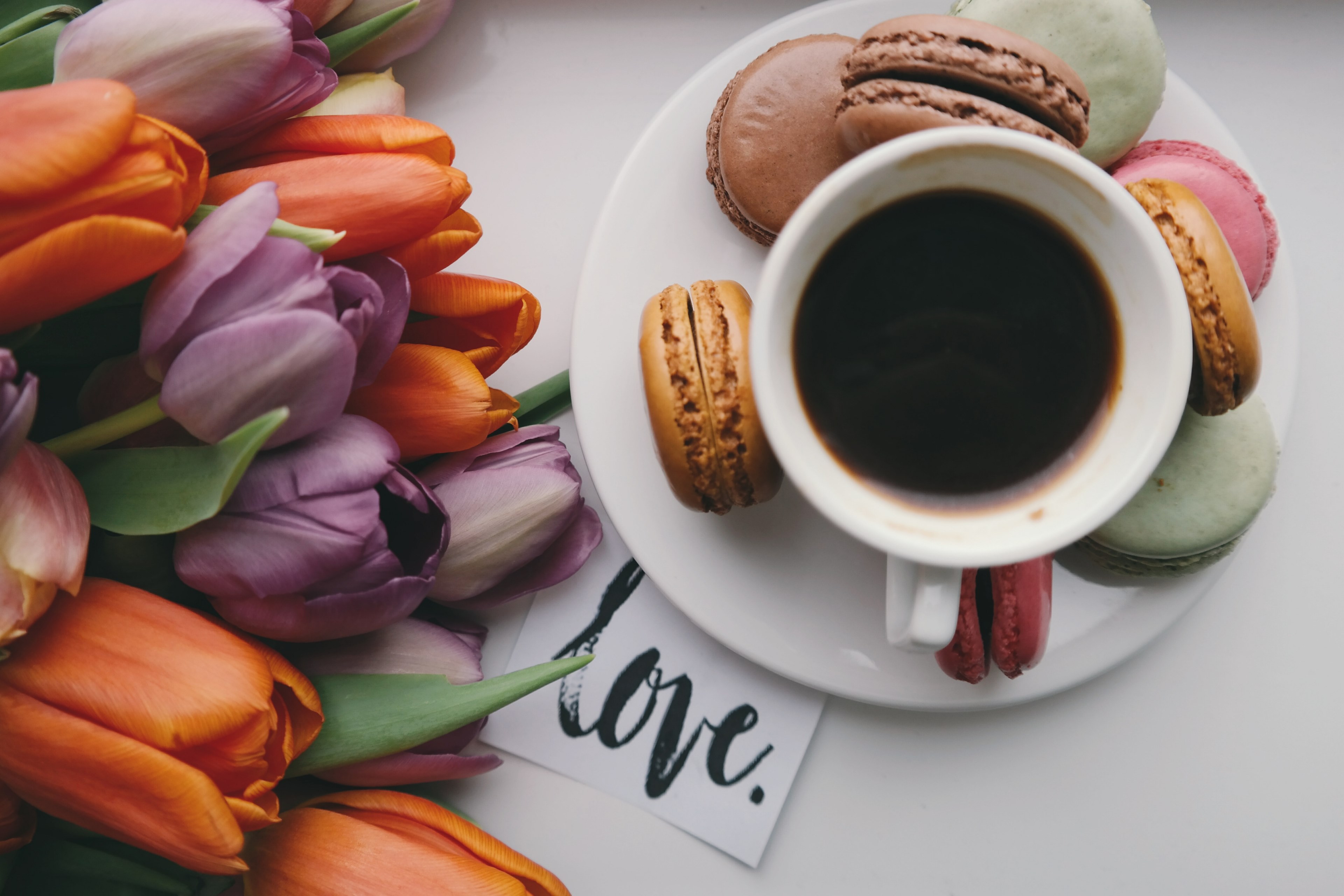 a black coffee in a small cup on top of a plate surrounded by flowers and snacks, _black coffee snacks 4k, HD Wallpaper