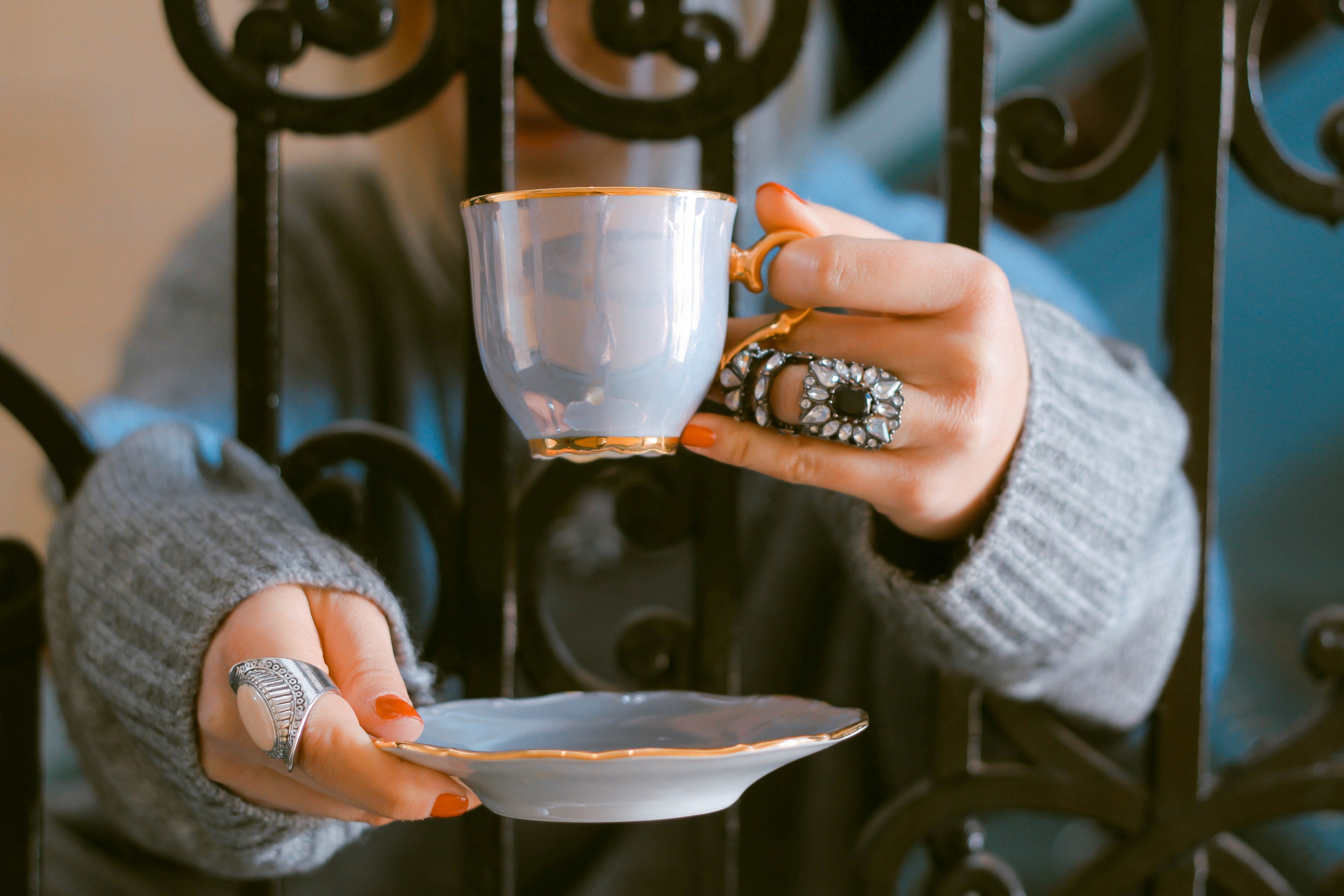 a woman wearing a grey oversized sweater and rings holding a blue ceramic cup and saucer while leaning on a gate in london, a woman is like a tea bag_ 4k, HD Wallpaper
