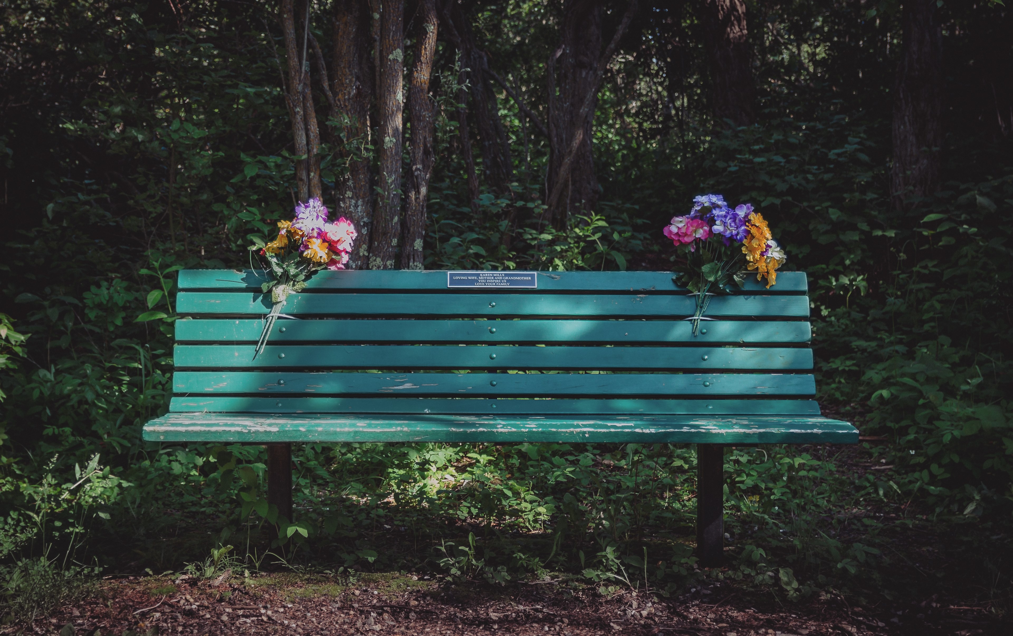 two colorful flower bouquets attached to a green park bench with a plaque on it, immortalized 4k, HD Wallpaper