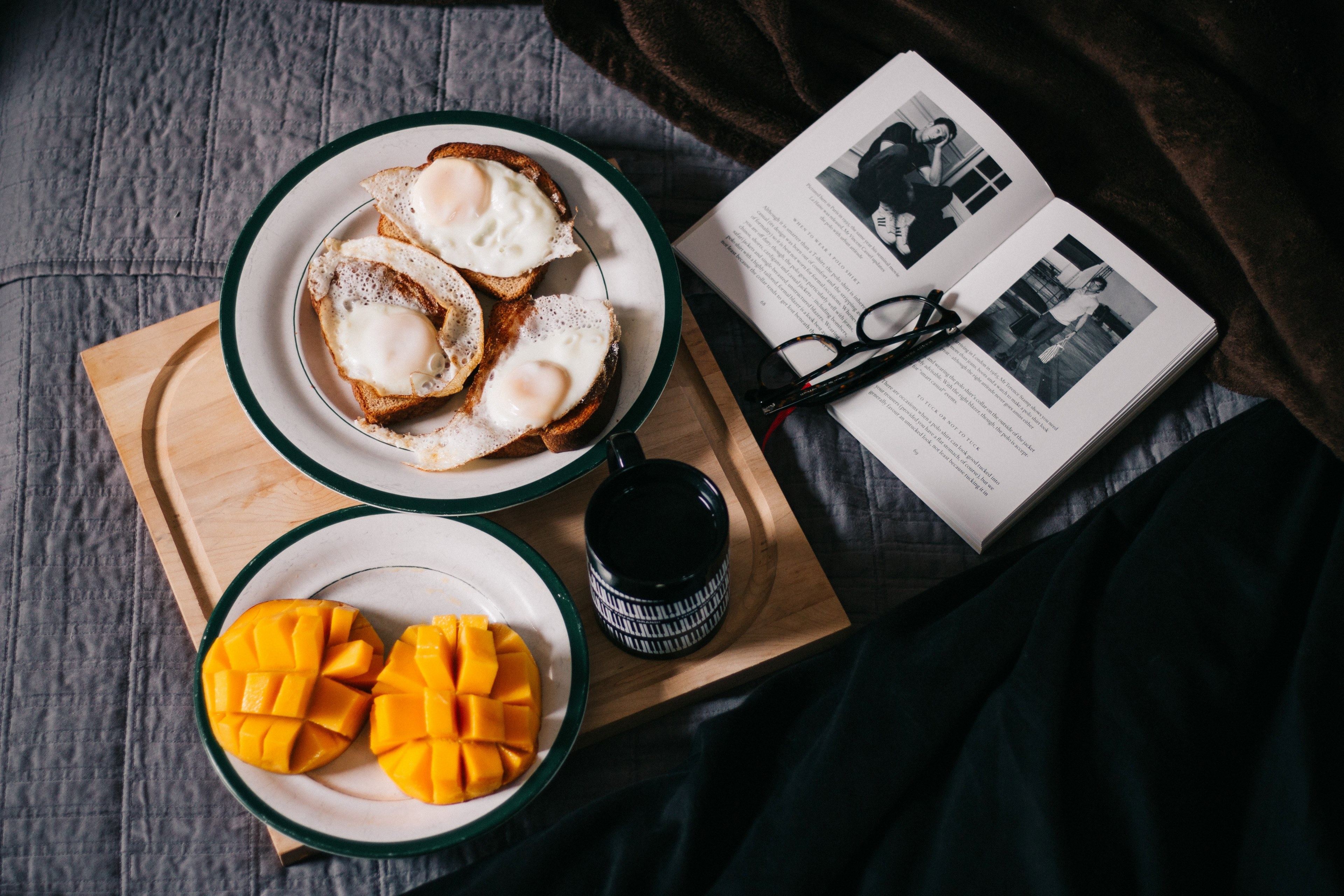 a breakfast spread including mango fried eggs and coffee on a wooden serving board next to a book and glasses on a bed, breakfast in bed 4k, HD Wallpaper
