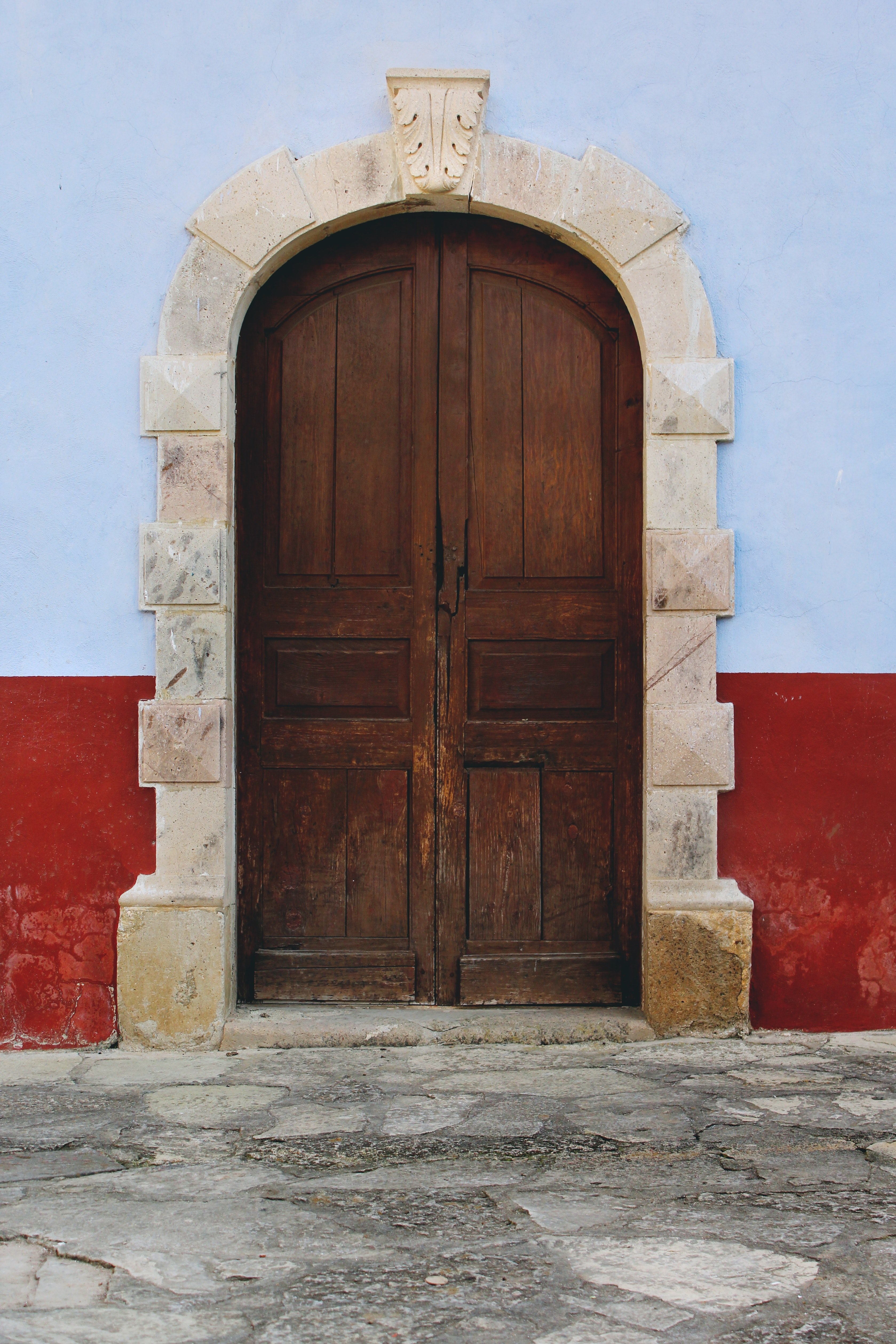 large domed wooden door with white stones on the border and a red and blue wall flanking it on a stone street, red and blue wall with wood door 4k, Phone HD Wallpaper