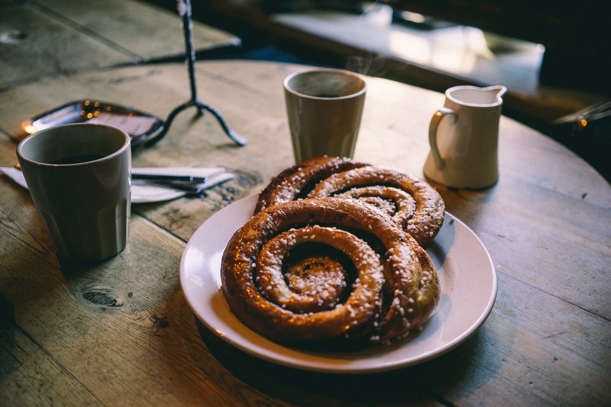 two large pastries on a white plate with two coffee mugs and cream on a round wooden table, pastries and coffee 4k, HD Wallpaper