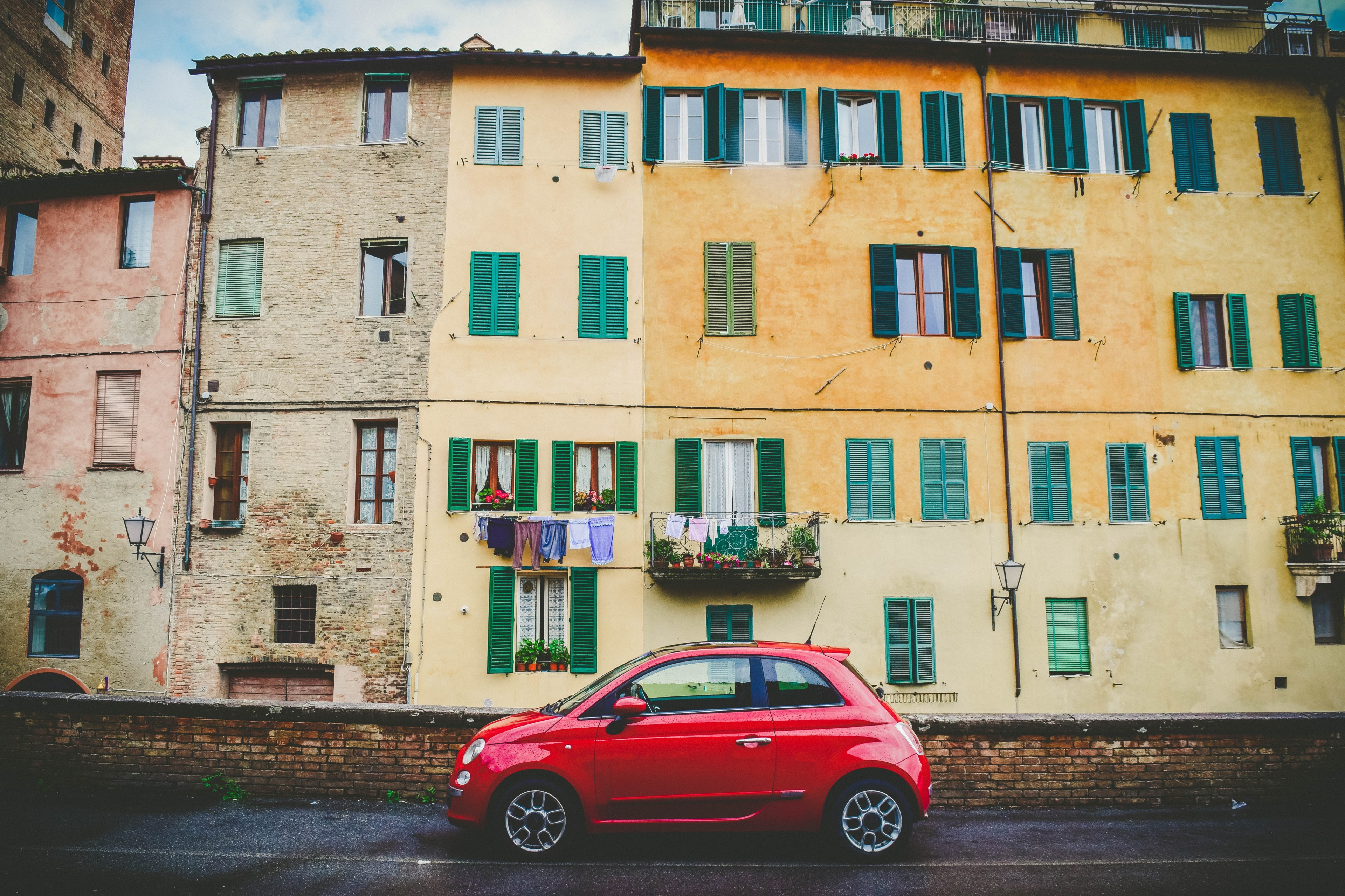modern red vehicle parked in front of traditional yellow apartments with green windows province of siena, red car yellow buildings 4k, HD Wallpaper