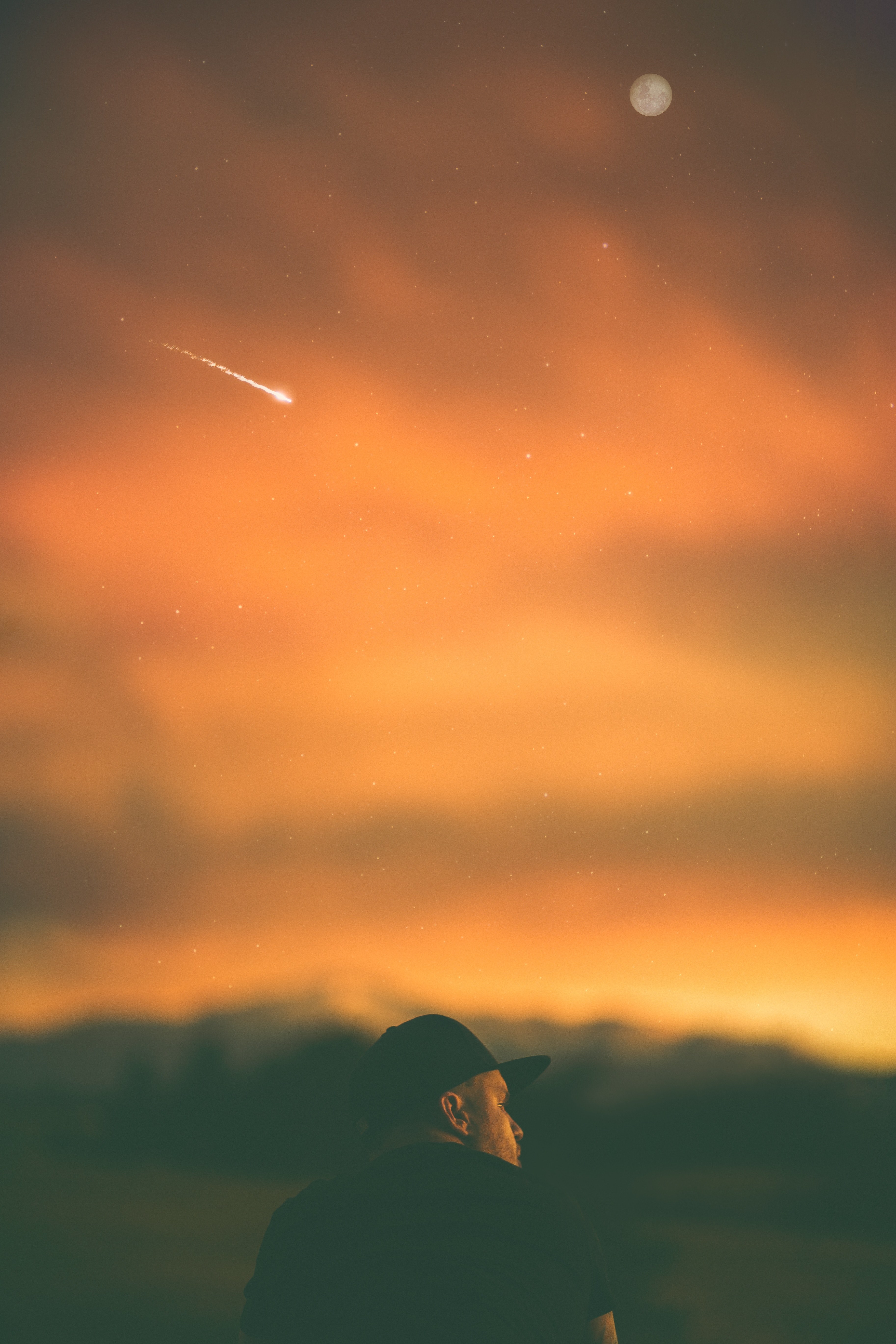 man sits beneath an orange sky where a meteor streaks and a full moon rises, man moon meteor at dusk 4k, Phone HD Wallpaper