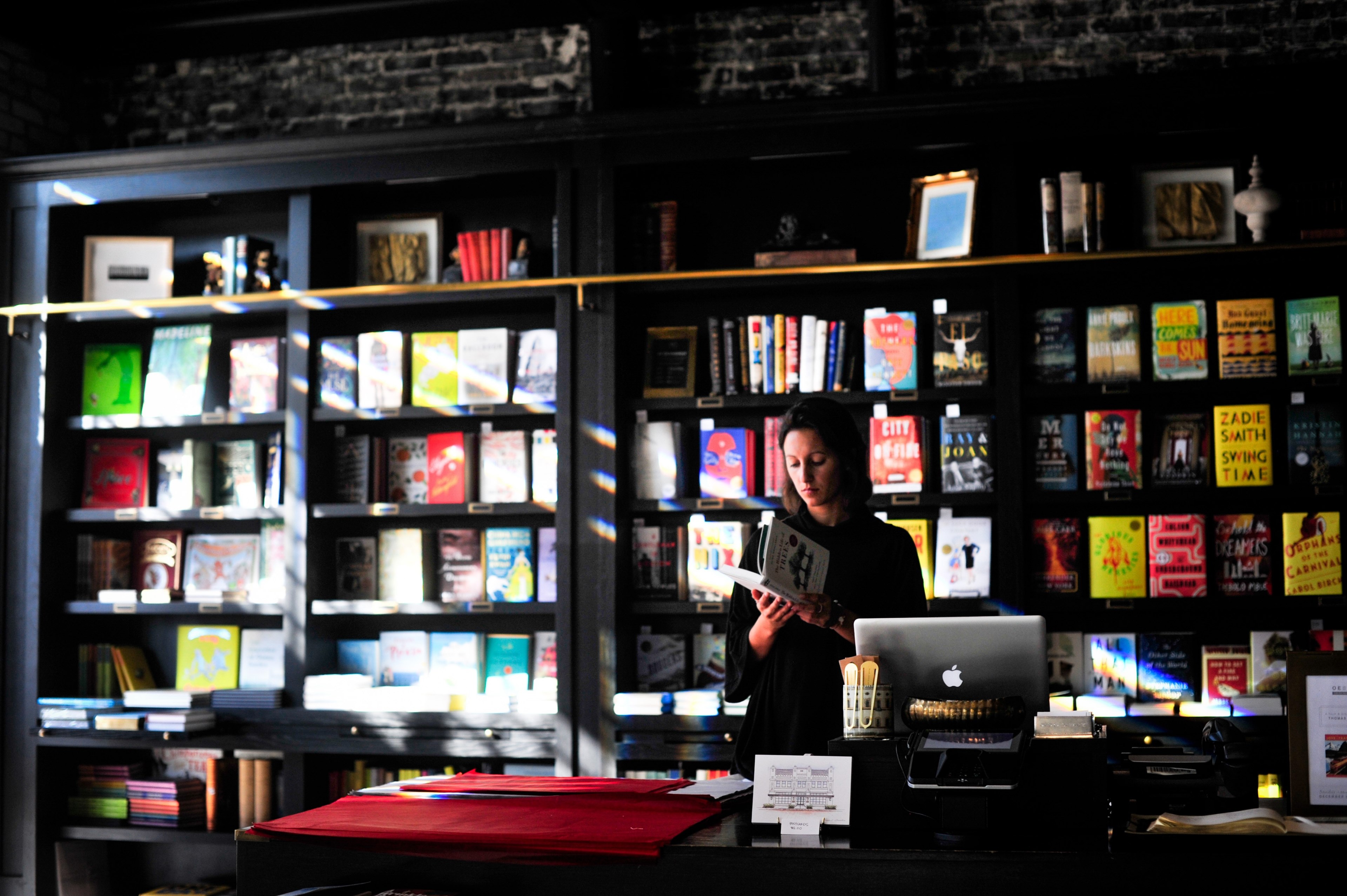 a woman skimming through a book while behind the cash register in a bookstore, lost in reading 4k, HD Wallpaper