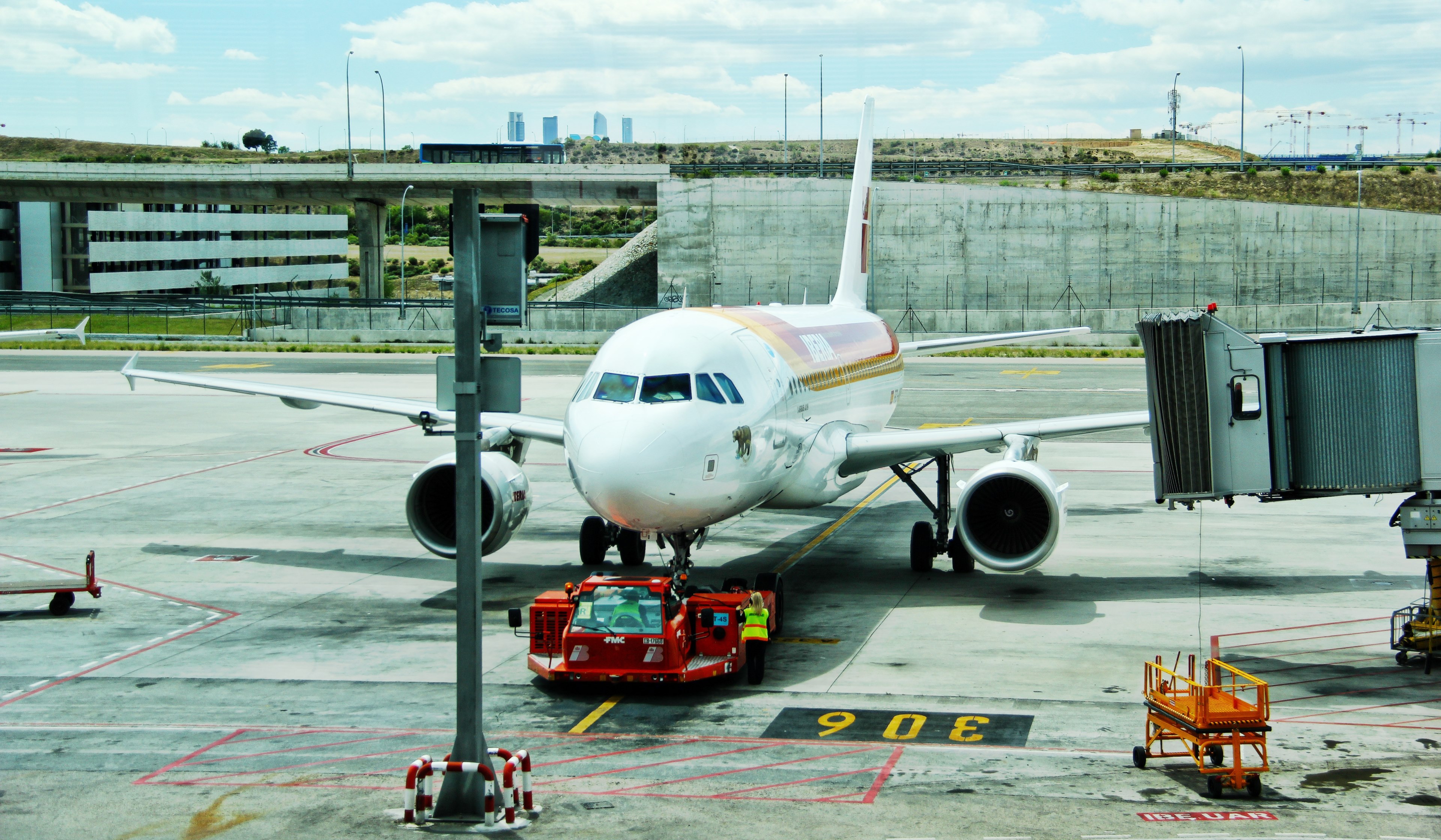 a white plane being pulled in from the runway by a vehicle with a developing city in the background, plane dragged on the tarmac 4k, HD Wallpaper