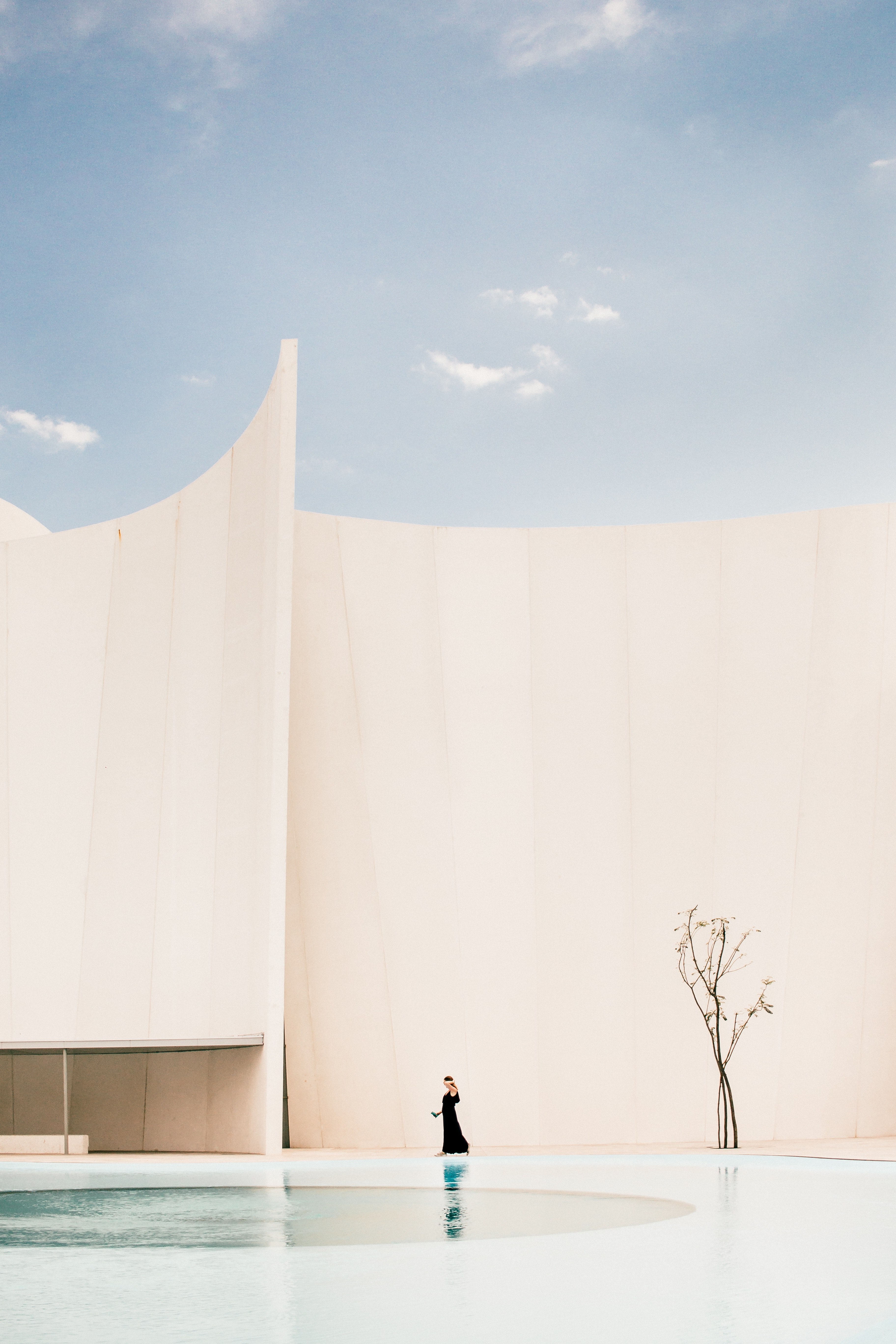 woman in a long black dress walking next to a swimming pool with a tall white wall in the background, lost in spaces without a return_ 4k, Phone HD Wallpaper