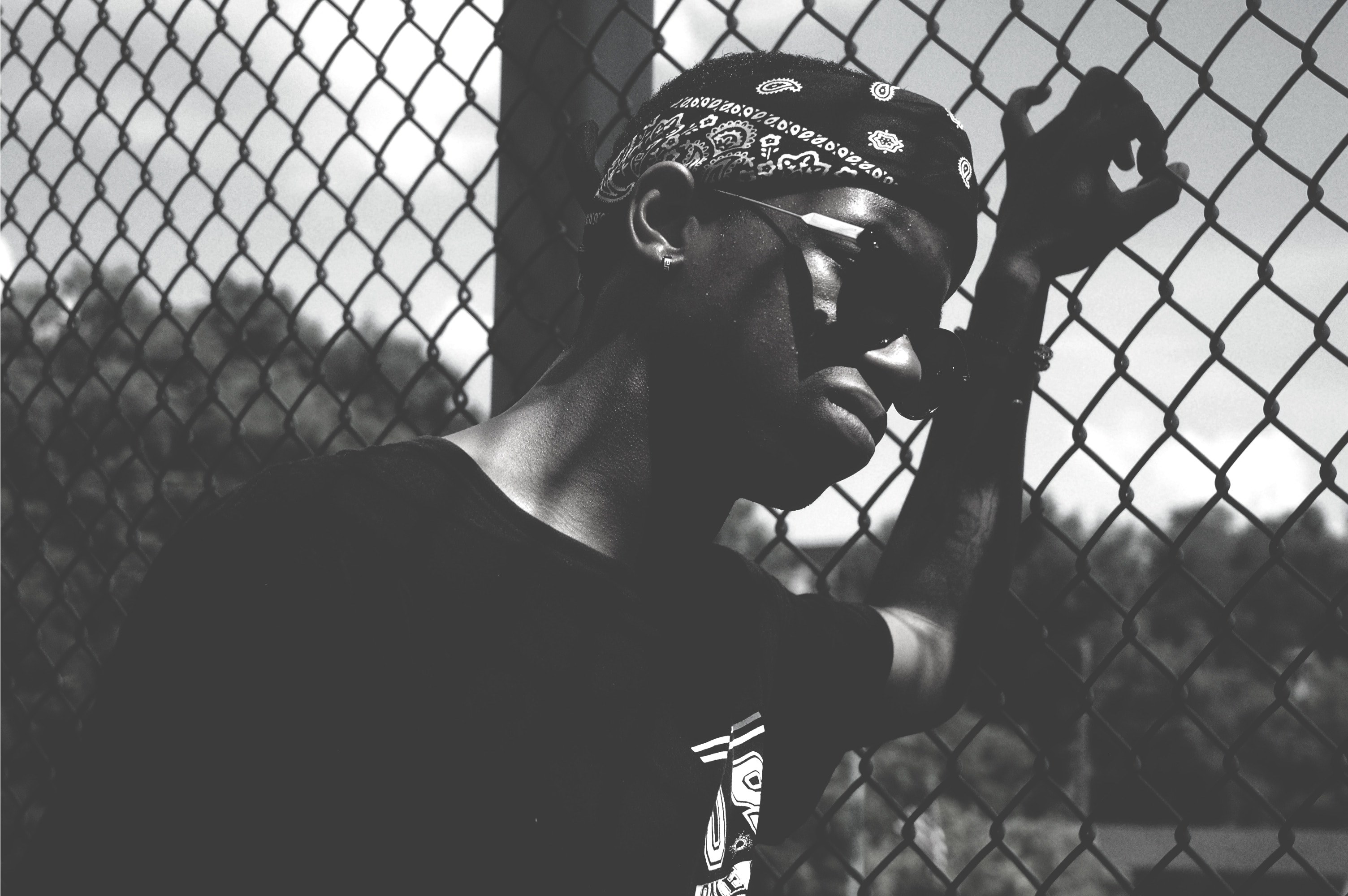 black and white shot of man in bandana with sunglasses leaning against wire fence in clarksville, man leans on wire fence 4k, HD Wallpaper