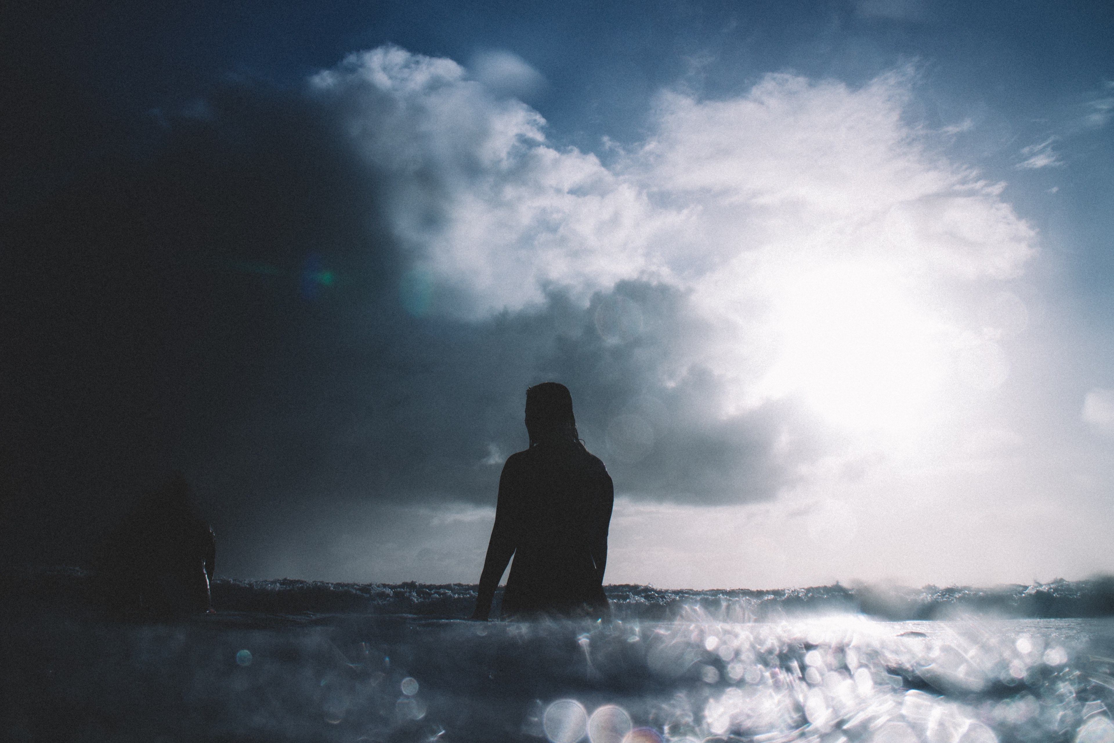 a silhouette shot of two surfers sat on their boards in the calm sea at piha beach as a cloud passes in front of the sun, surfers sitting on boards 4k, HD Wallpaper