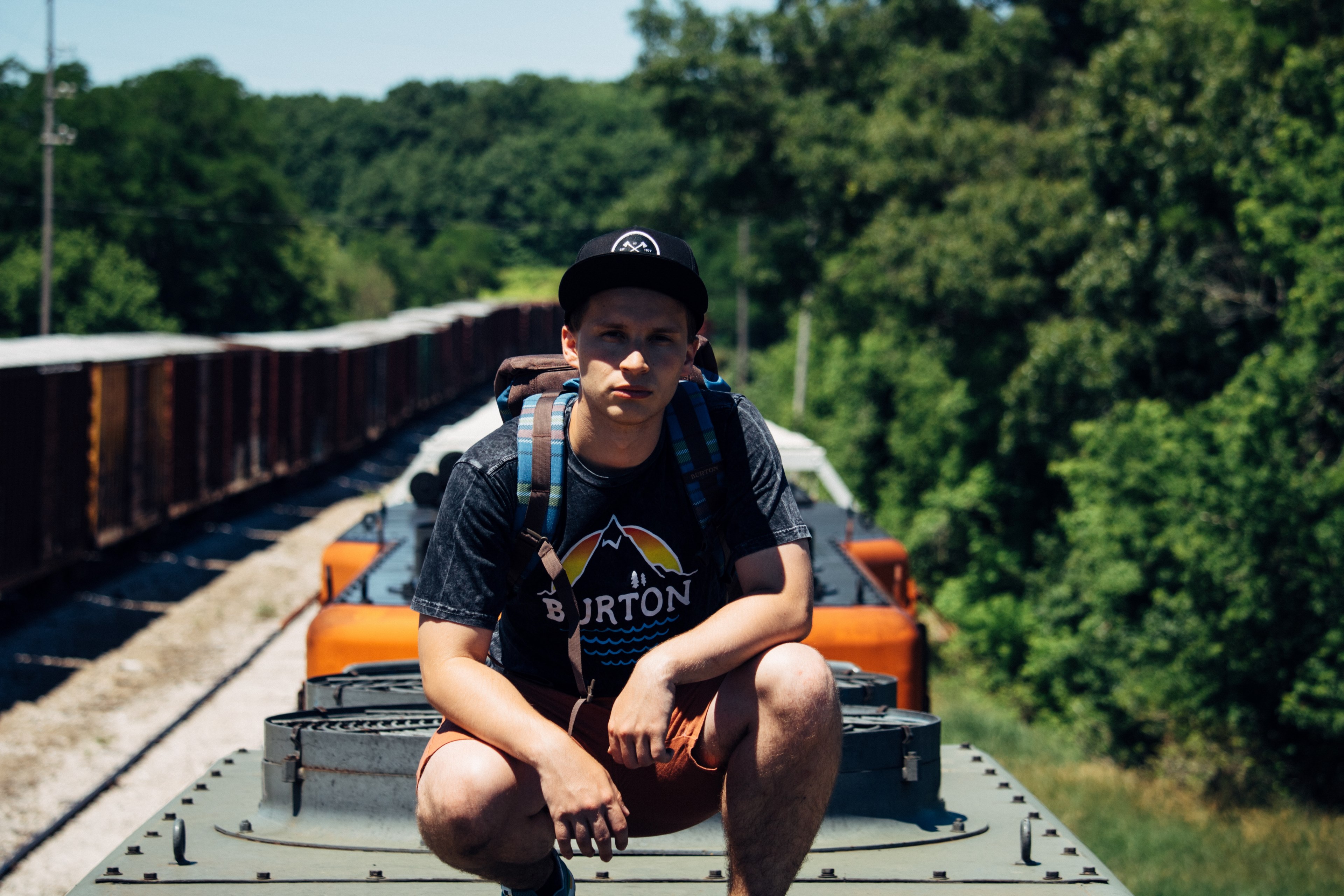a young male backpacker in a hat crouching on top of a train, train surfing backpacker 4k, HD Wallpaper
