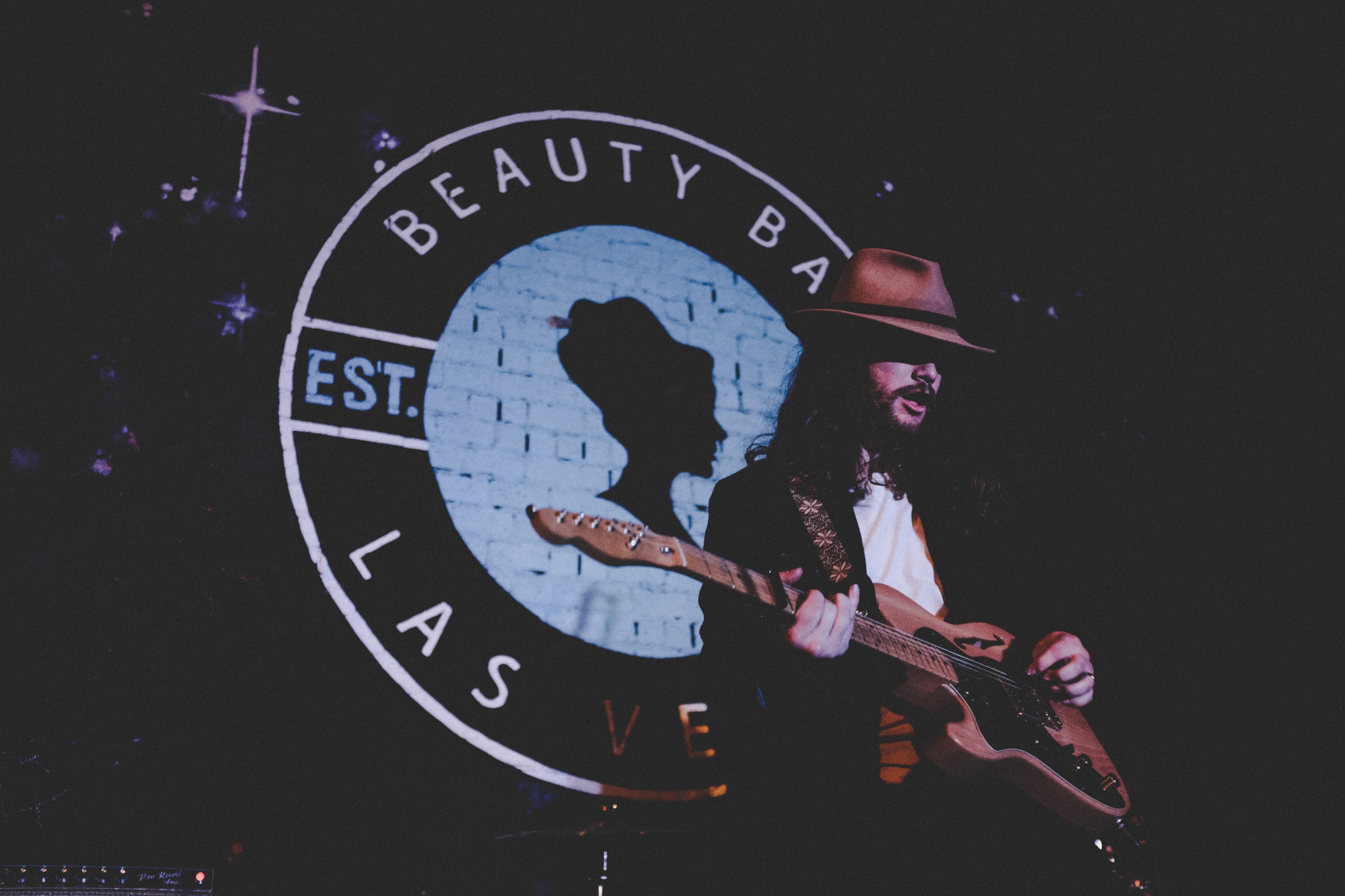 a flamboyant man playing a guitar in front of a beauty bar las vegas logo, exuberant guitar player 4k, HD Wallpaper