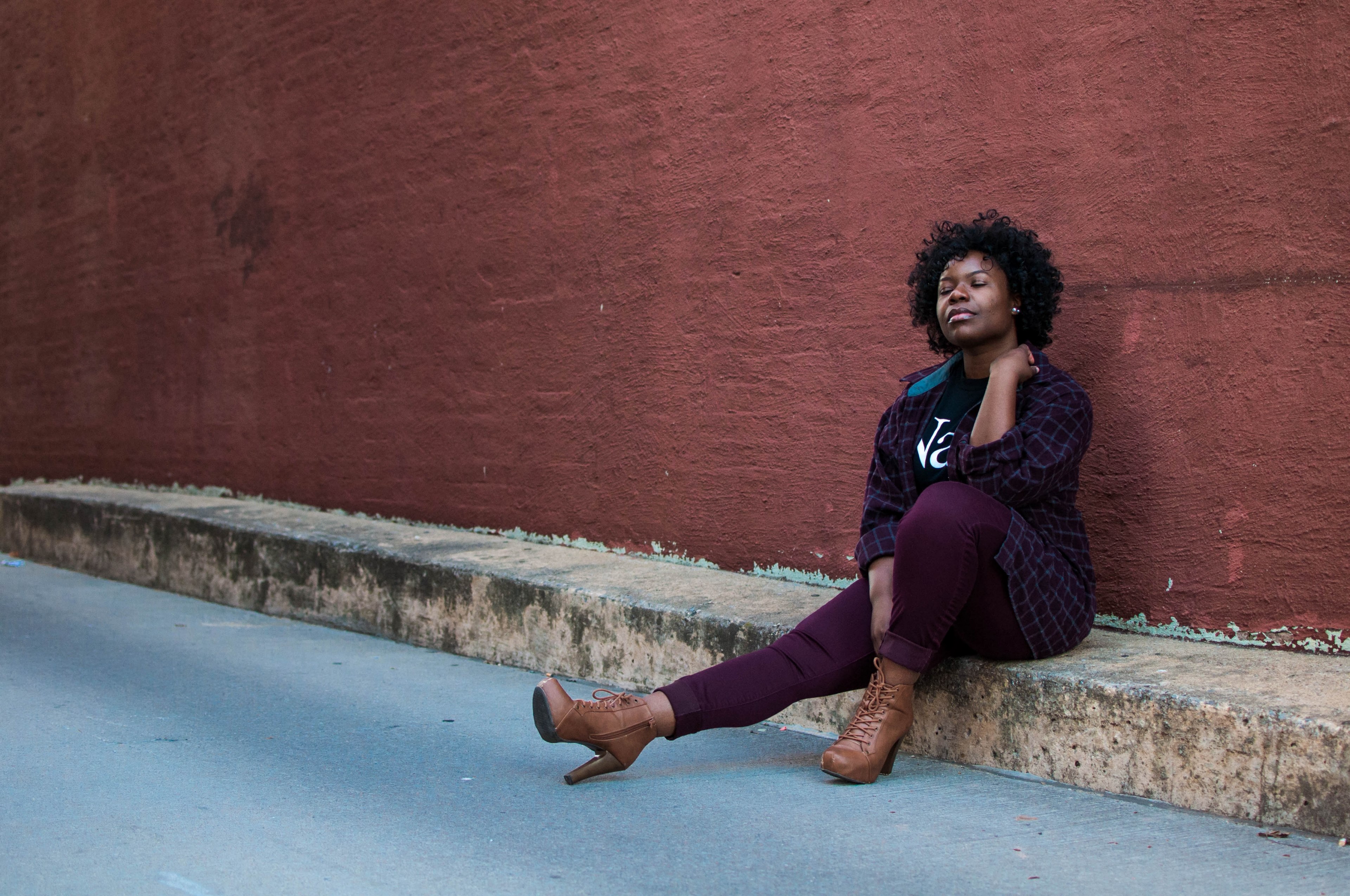 woman in brown boots sits with one leg out on a curb aside a red wall, woman sitting on curb 4k, HD Wallpaper