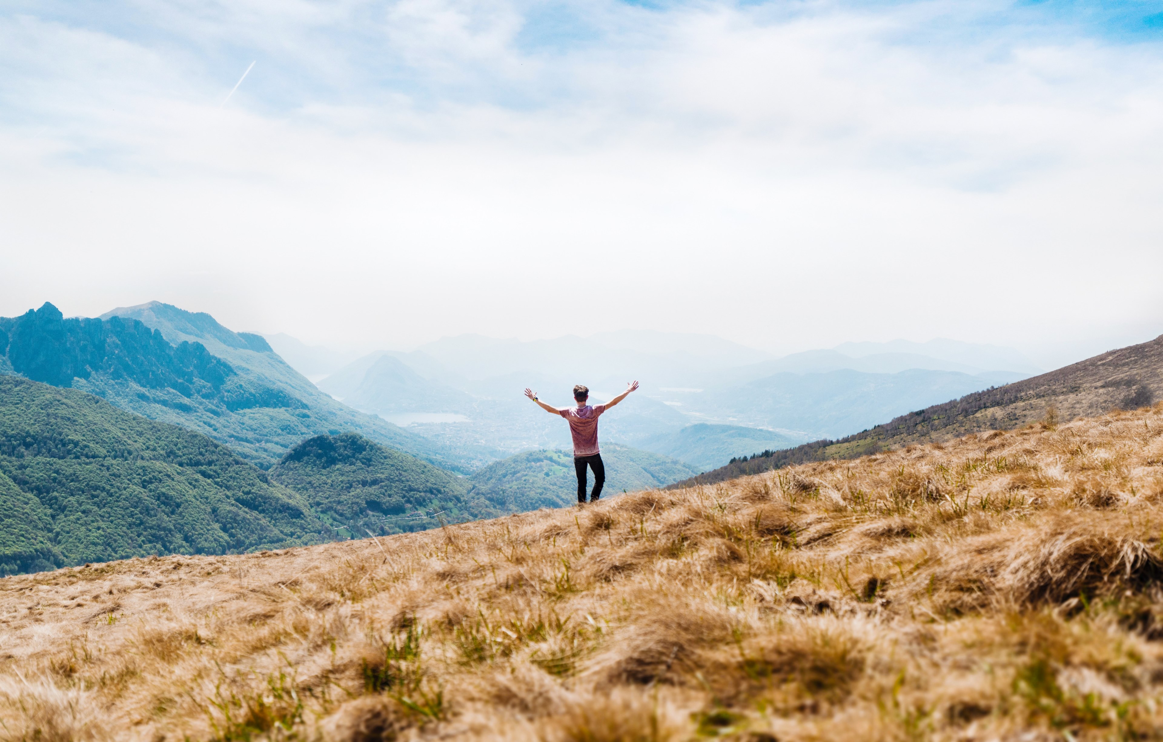 a man stands with his arms outstretched on a grassy slope in the mountains, enjoying freedom in the mountains 4k, HD Wallpaper