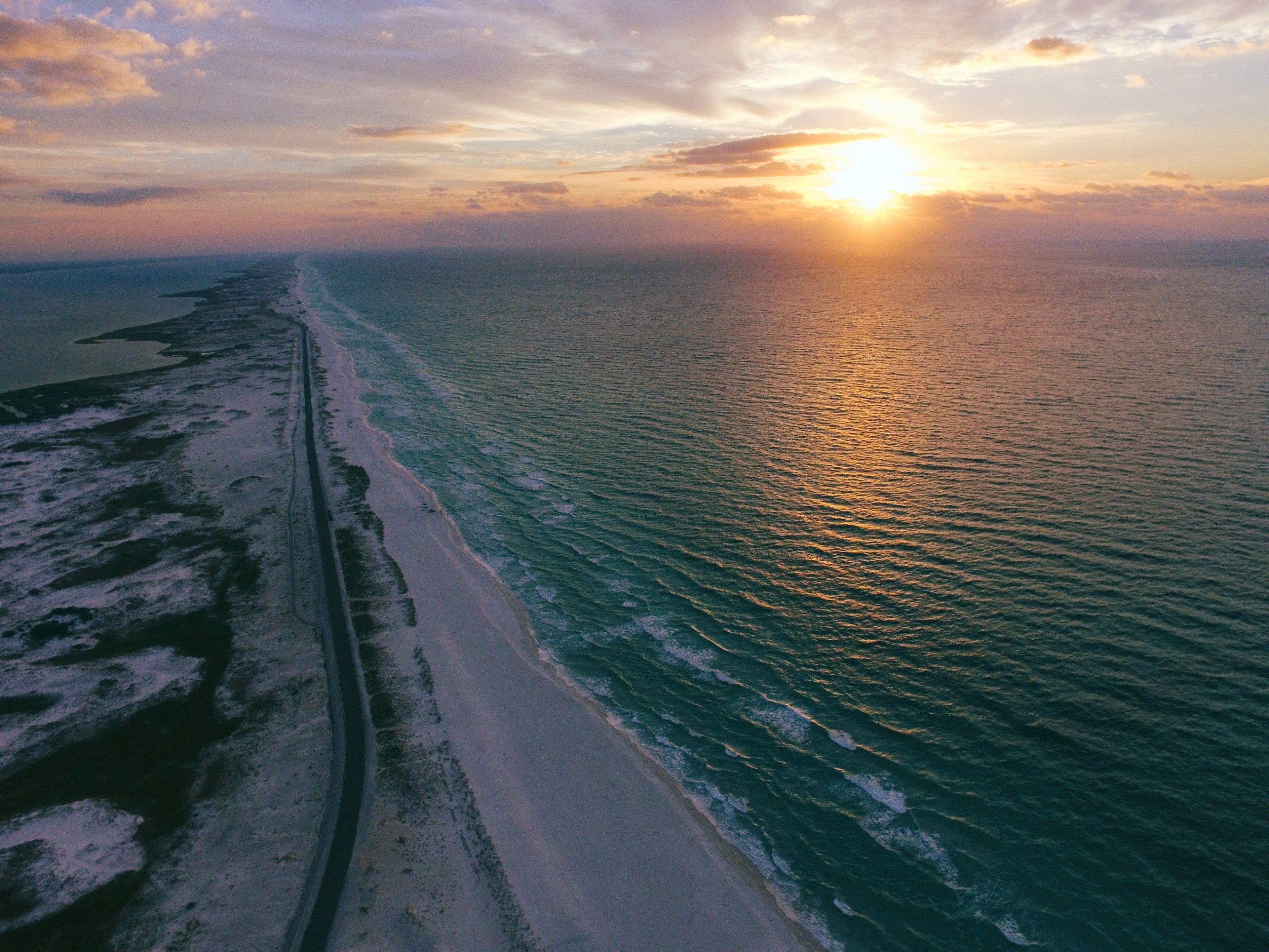 drone view of an empty coastal road beside the beach sun setting over rippling water, sunrise sunset drone view and aerial view 4k, HD Wallpaper