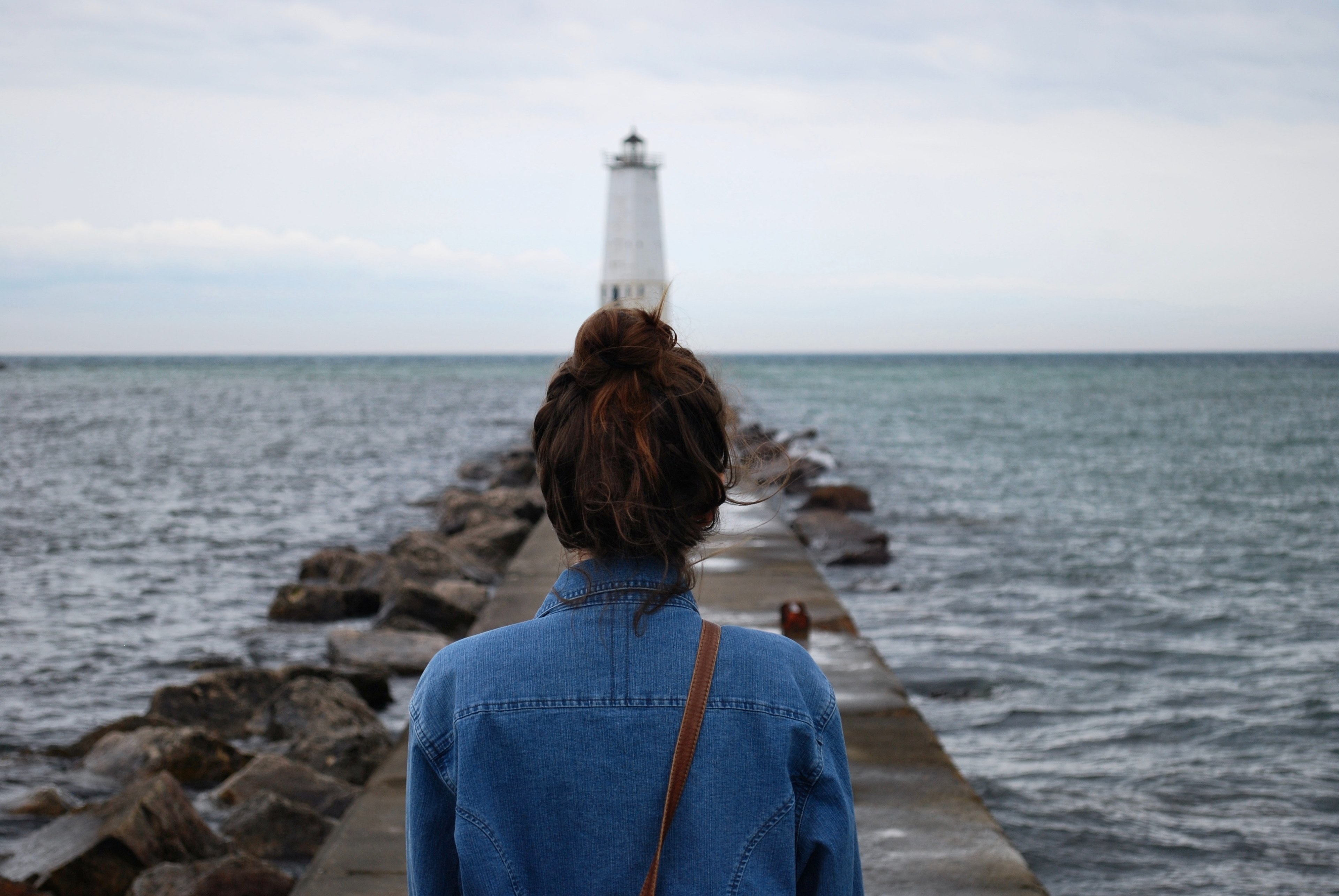 a woman in a bun walks down a rocky pier on the ocean toward a lighthouse, woman walking to lighthouse 4k, HD Wallpaper