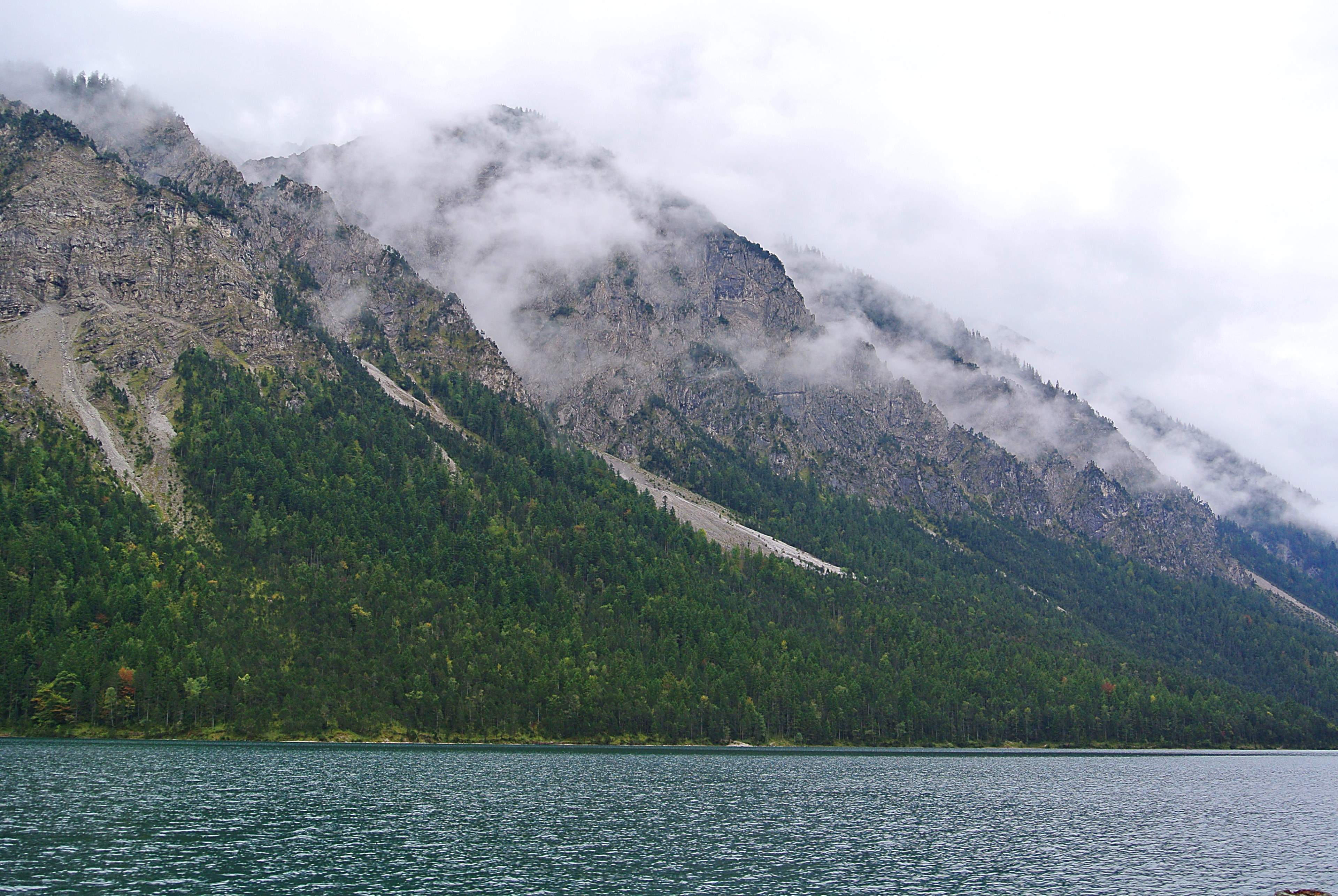 rocky mountains with cloud shrouded peaks stretch along the shore of a tranquil lake, misty mountains along the lake 4k, HD Wallpaper