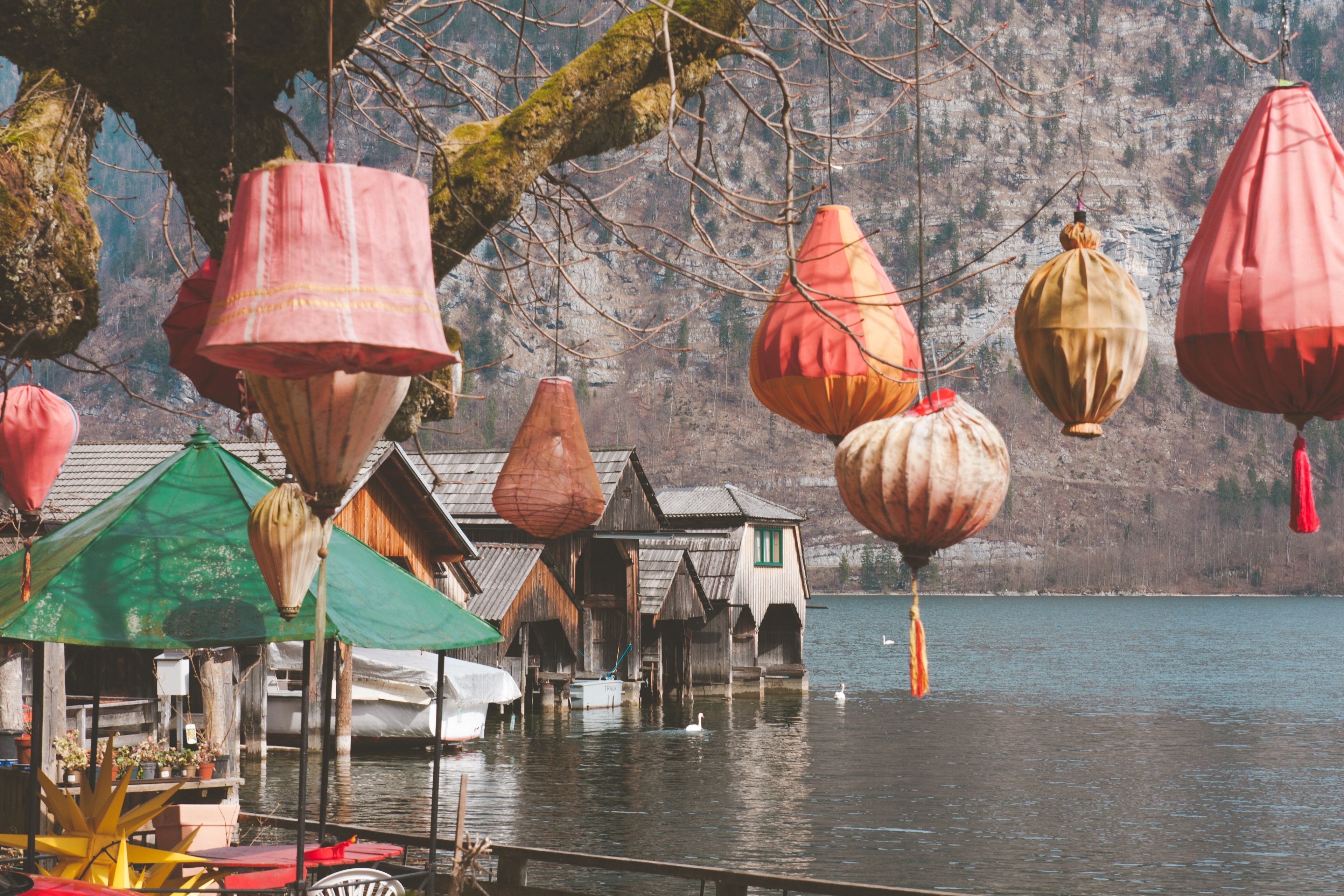 wooden buildings sitting on lake hallstatt framed with red and orange lanterns hanging from a tree, dream 4k, HD Wallpaper