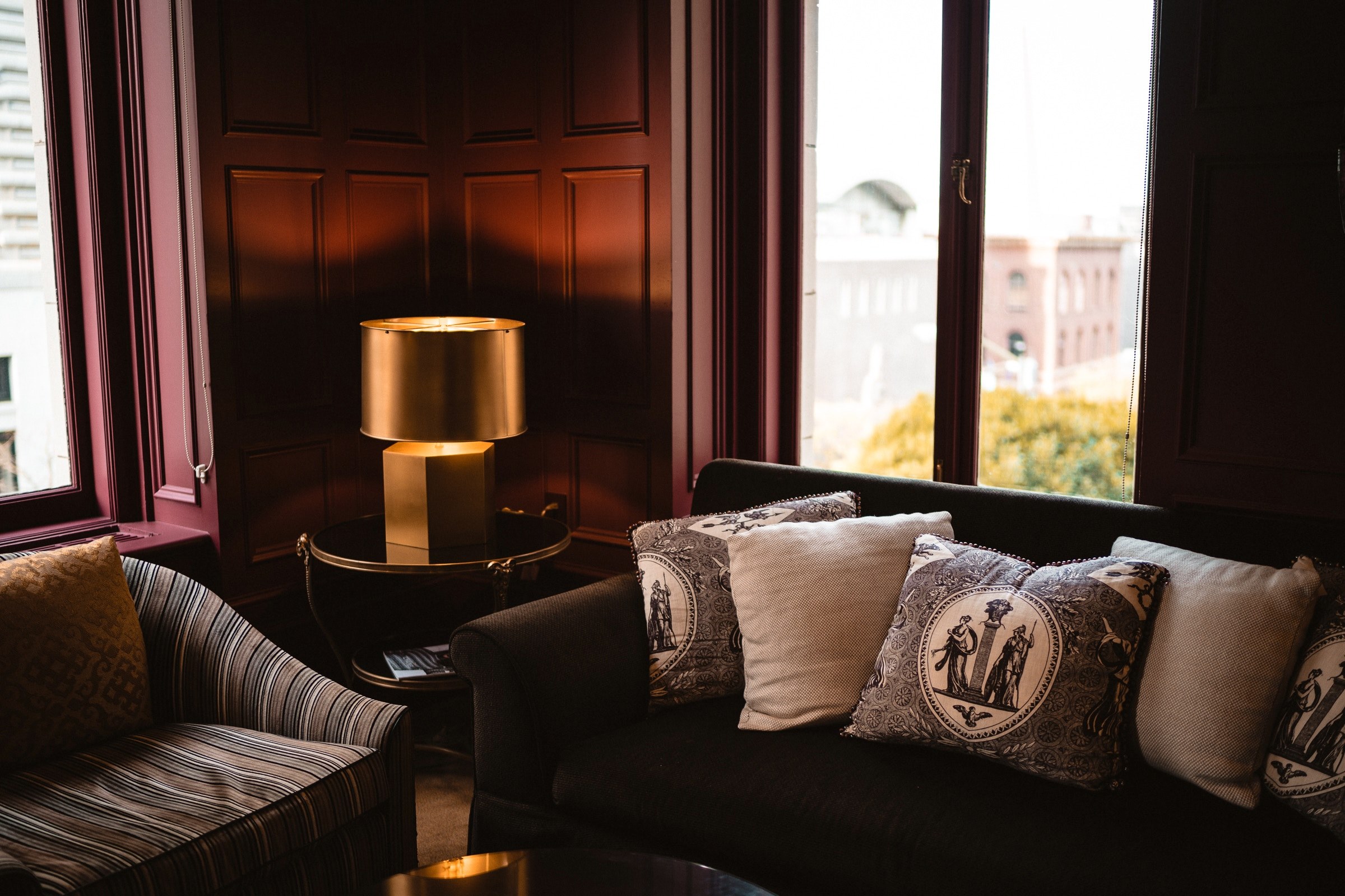 corner of a room with a gold lamp two couches and decorative pillows overlooking brick buildings, corner of room with lamp 4k, HD Wallpaper