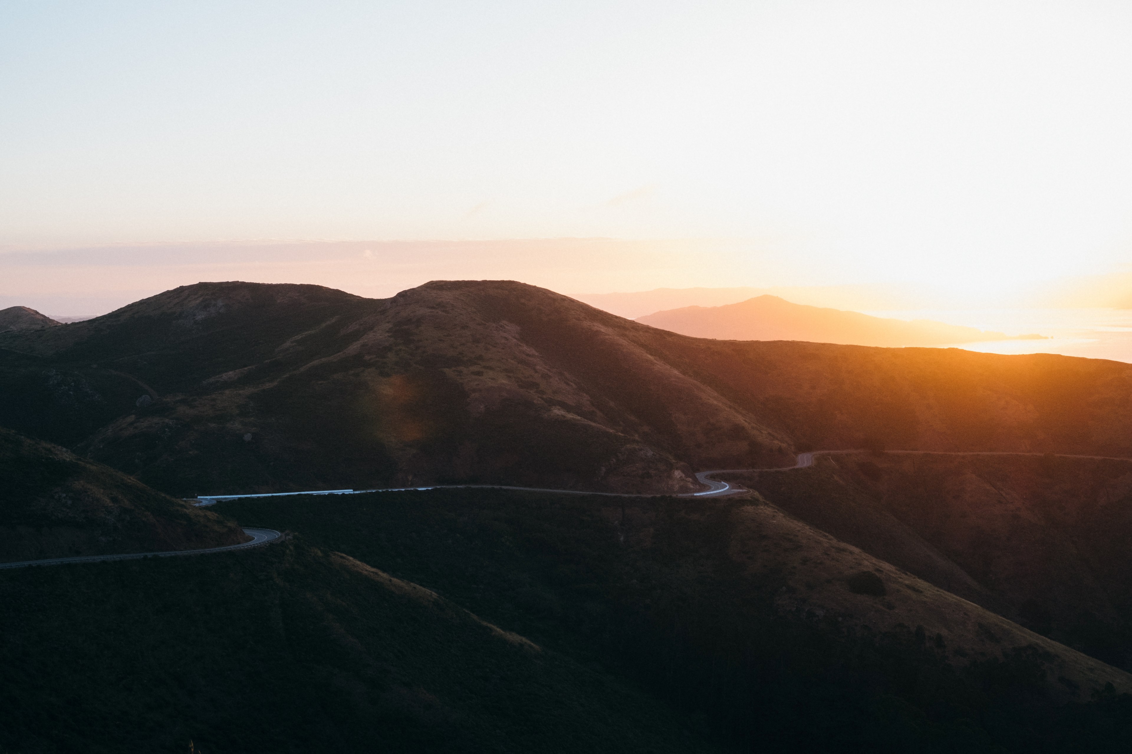 a winding road on a mountain range the sun setting in the distance, mountain sunset sunrise and golden hour 4k, HD Wallpaper